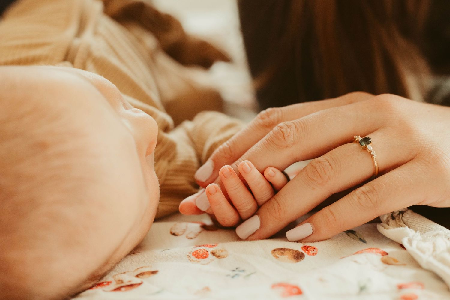 Mother gently holding newborn baby's tiny hand, wearing a delicate diamond engagement ring.