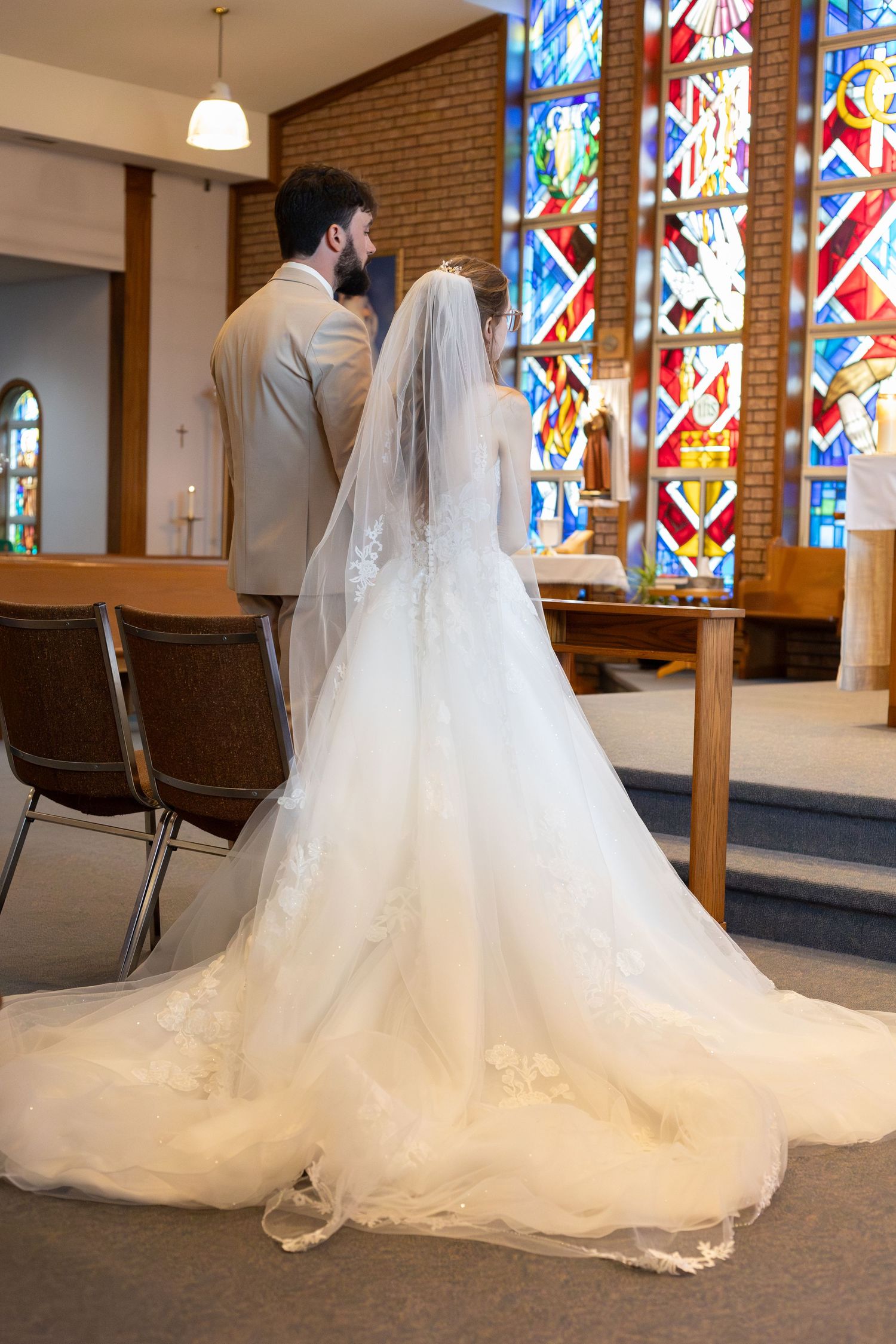 Bride and groom standing at church altar with colorful stained glass windows during wedding ceremony.