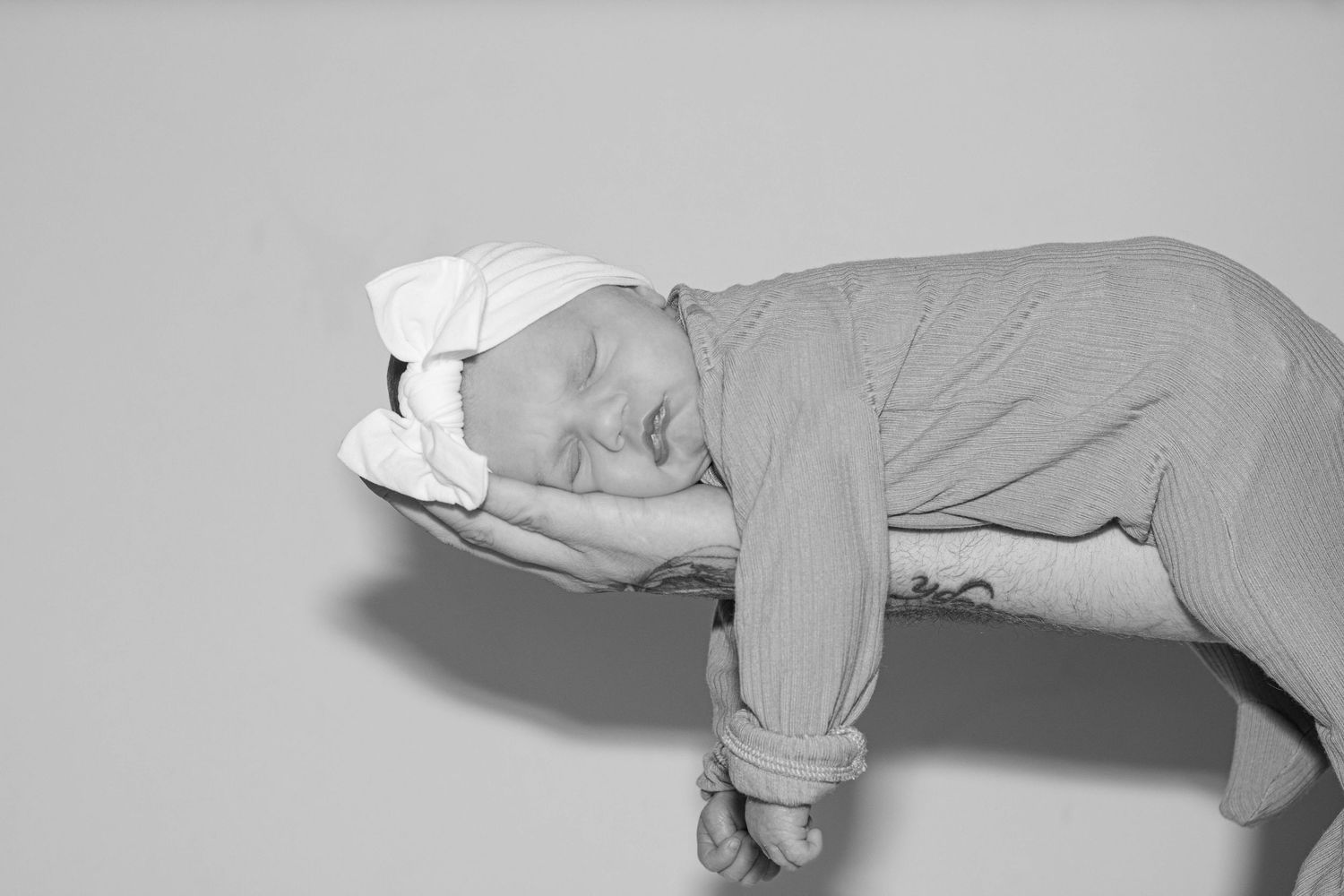 Black and white photo of sleeping newborn baby in striped outfit with white bow headband.