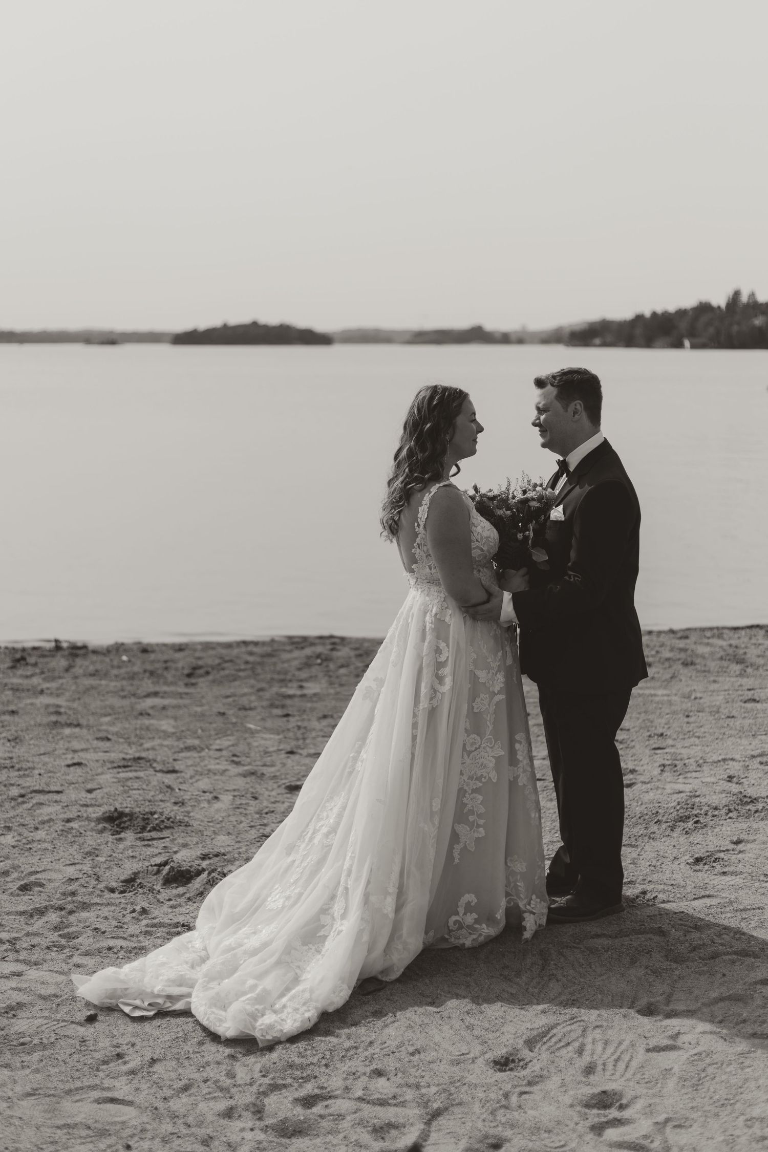 Bride and groom share an intimate moment on a sandy beach in black and white.