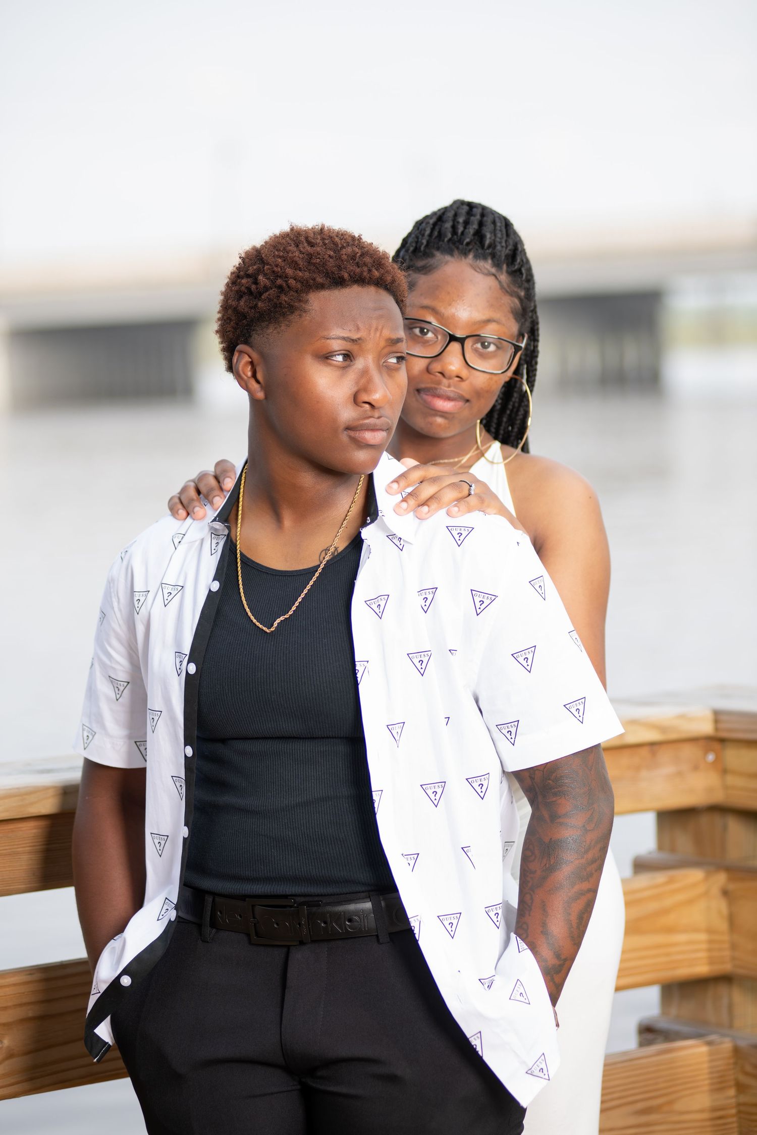 Couple posing on a waterfront dock, woman with braids resting hands on partners shoulders.
