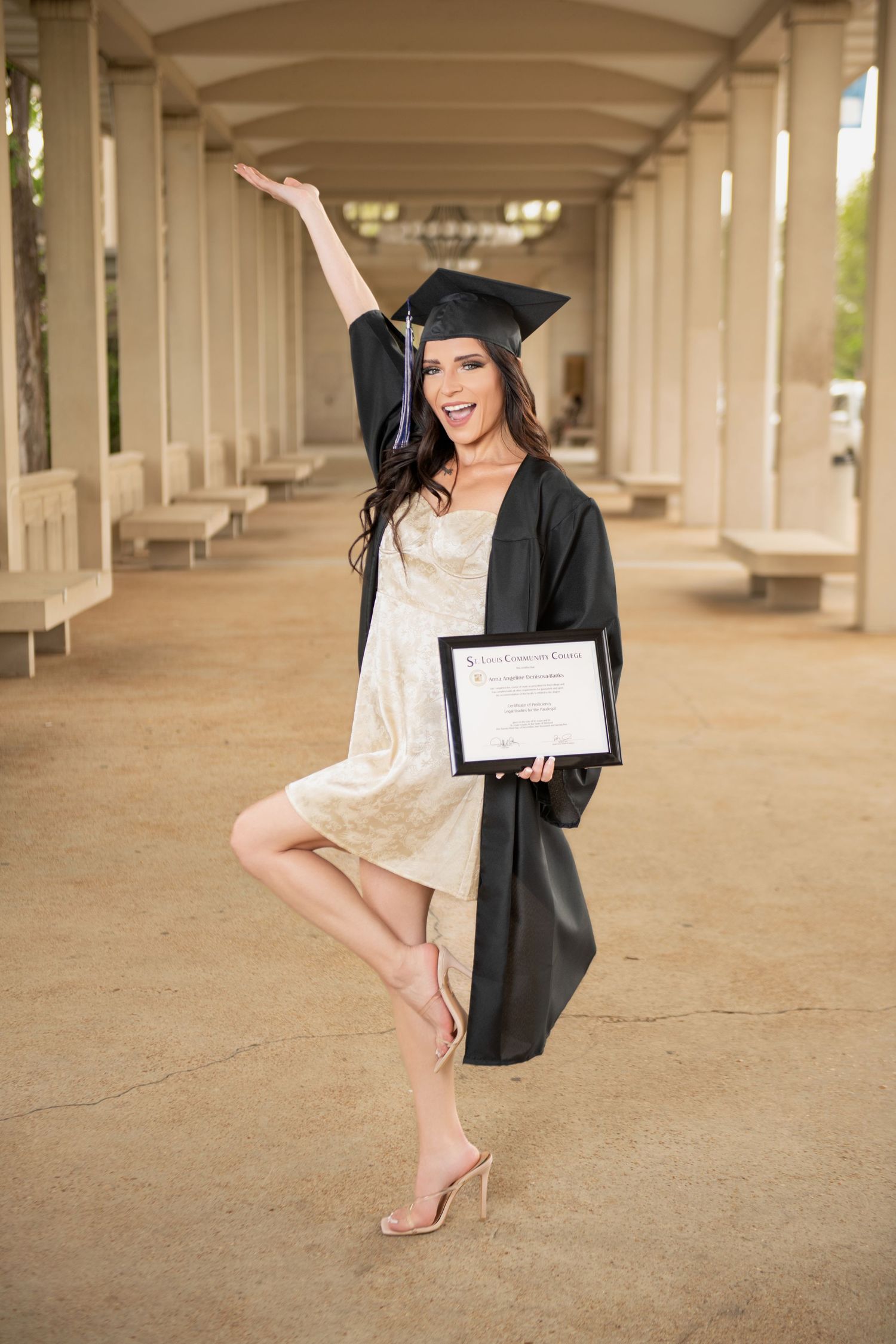 Excited graduate in cap and gown holding diploma with arm raised celebrating outdoors.