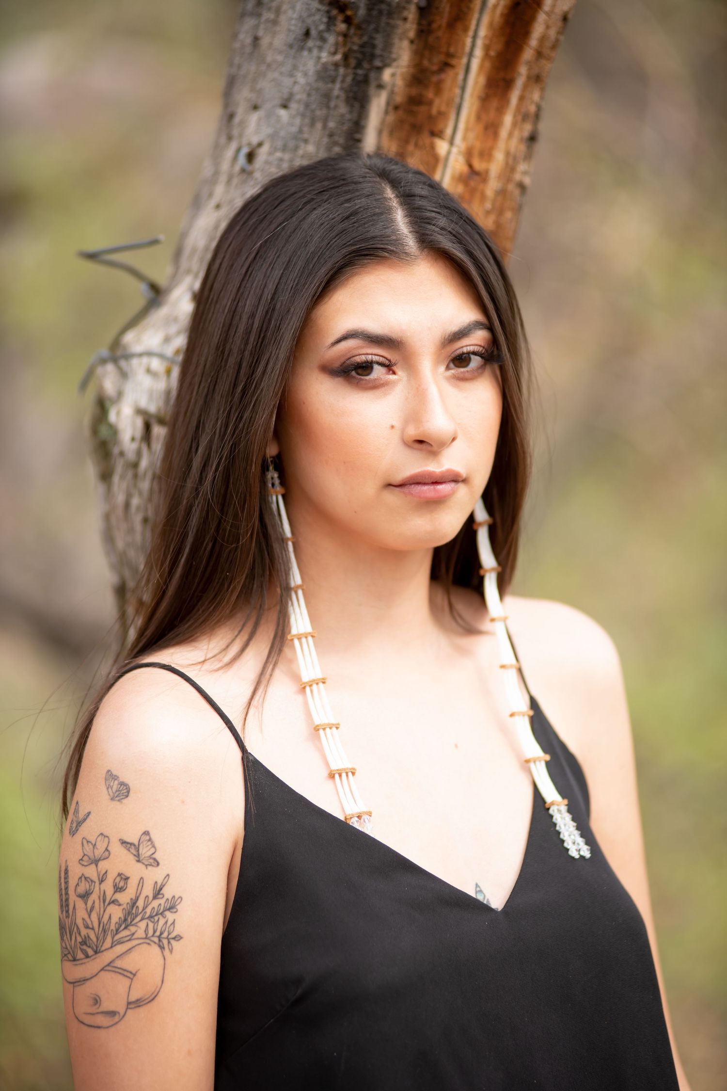 Young woman with long dark hair wearing a black dress and traditional Native American jewelry outdoors.