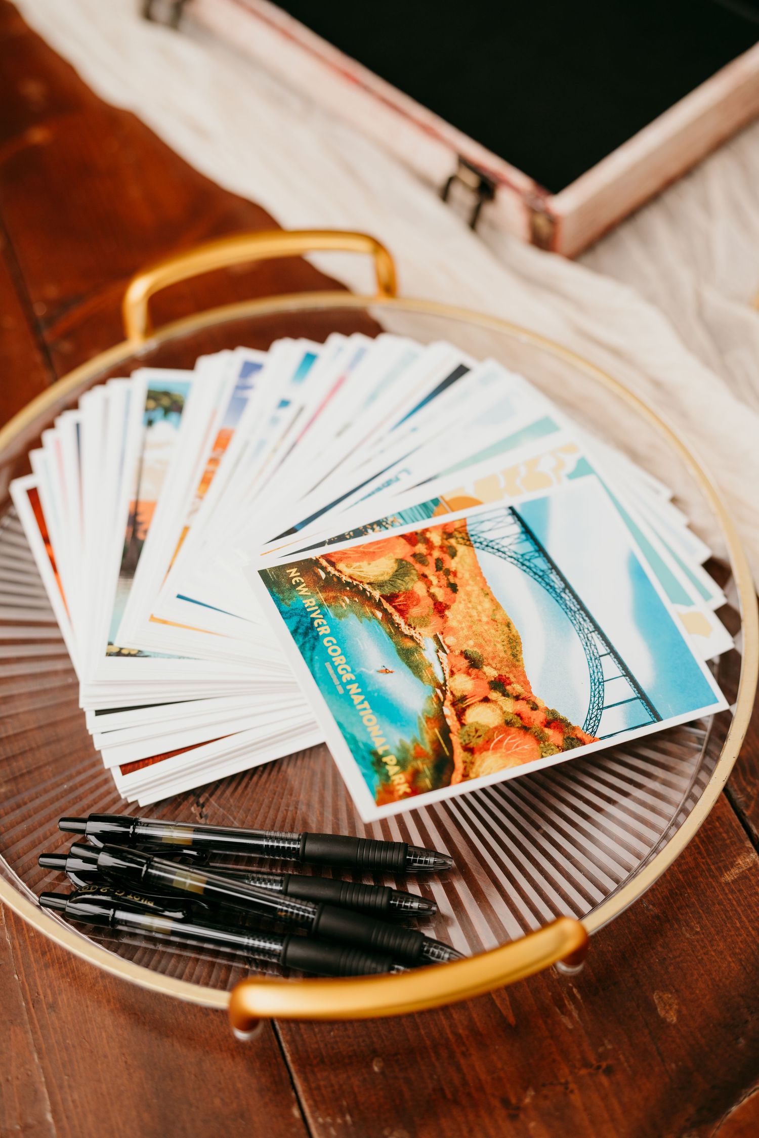 Stack of postcards and pens arranged on a circular wooden tray in warm lighting.