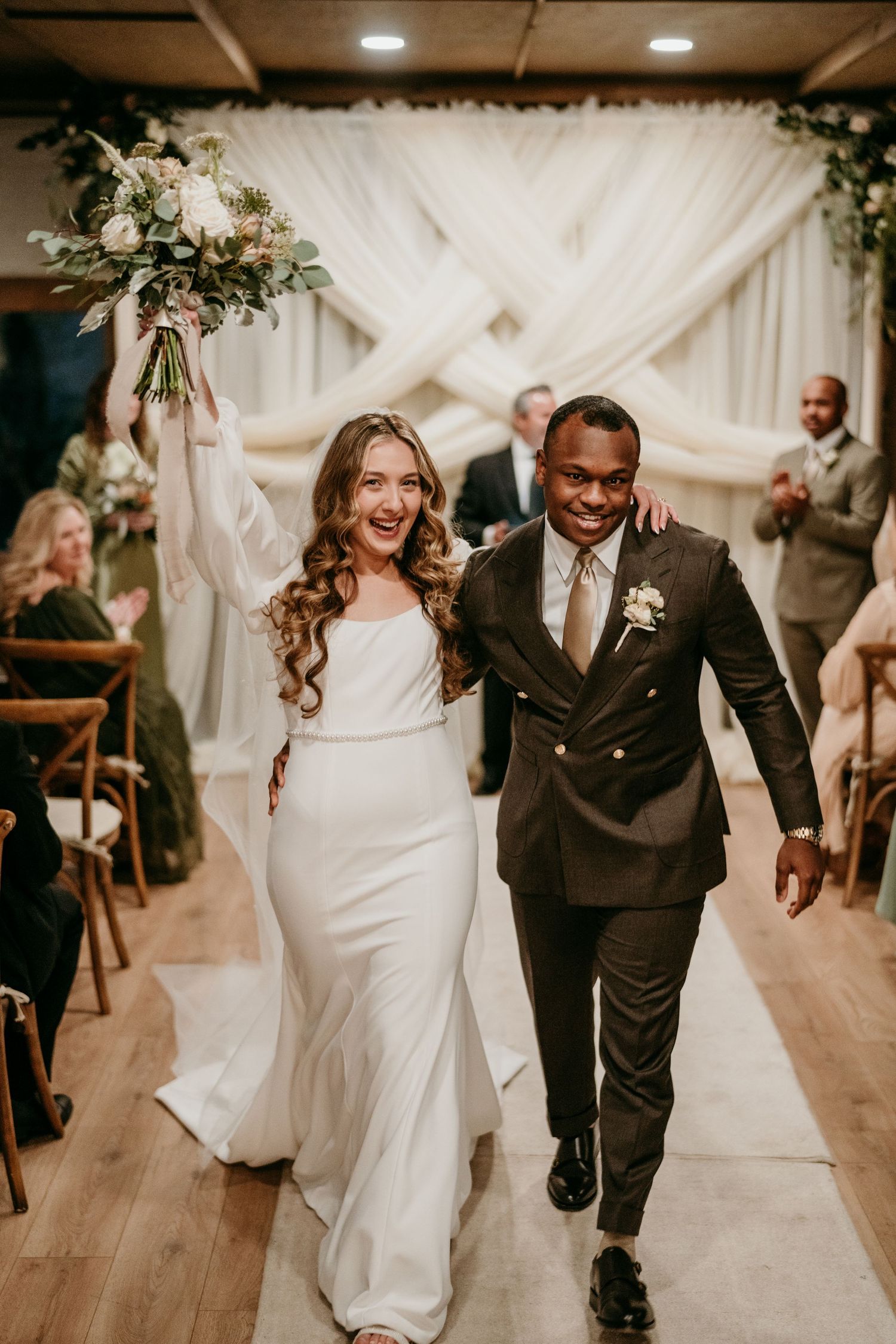 A couple walks joyfully down the aisle after their wedding ceremony in front of an elegant white draped backdrop in Nashville TN