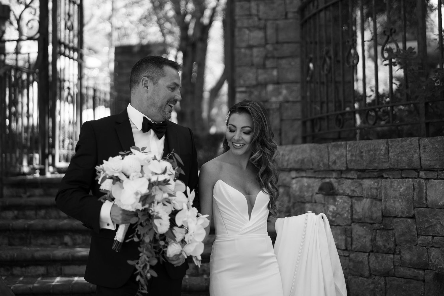 A black and white wedding photo shows a couple with white bouquet standing by stone stairs and iron railing in Nashville TN