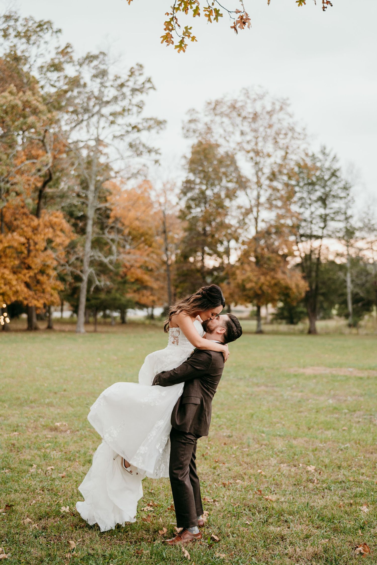 A couple embraces in a romantic autumn scene with falling leaves and golden trees in the background.