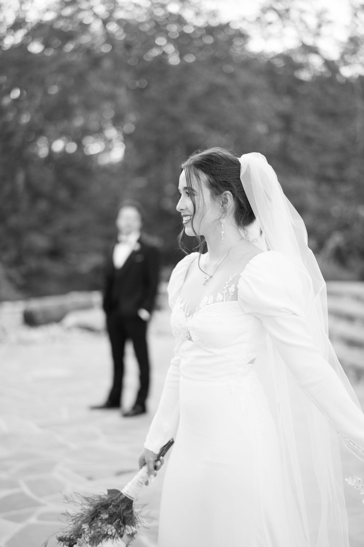 Elegant wedding scene outdoors with flowing white gown and veil against natural background.