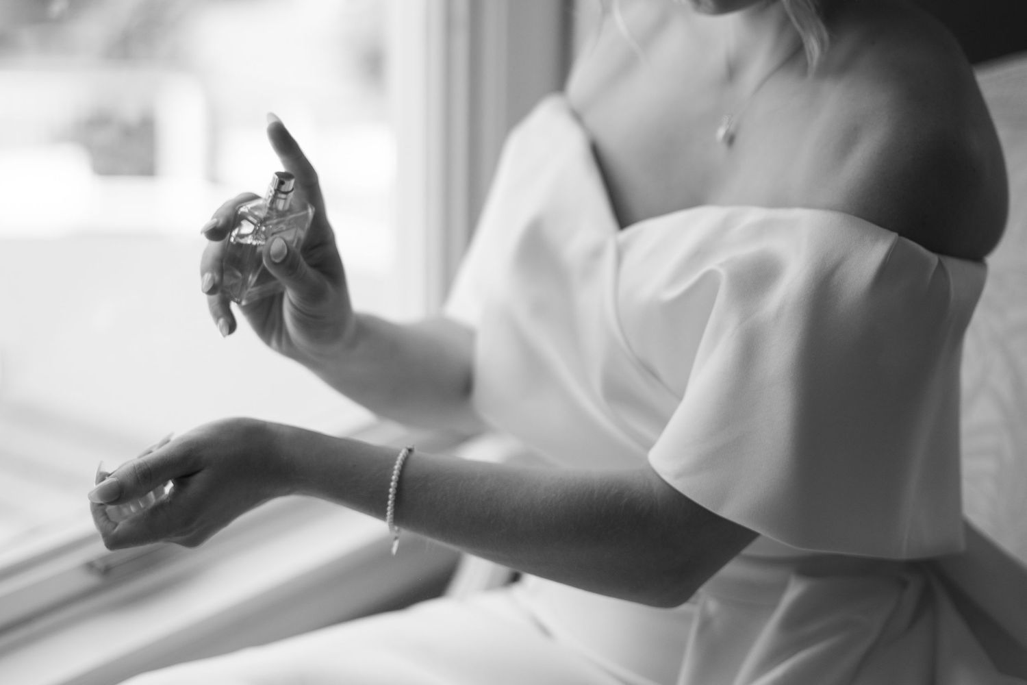 Elegant close-up of hands in white bridal dress sleeve by window light.