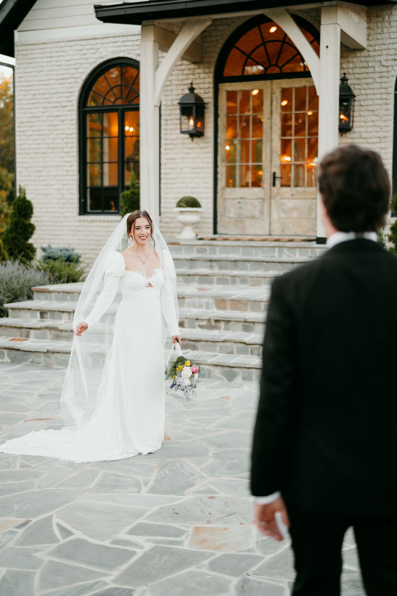 Beautiful wedding scene outside white stone chapel with elegant stairs and arched doorway at dusk.