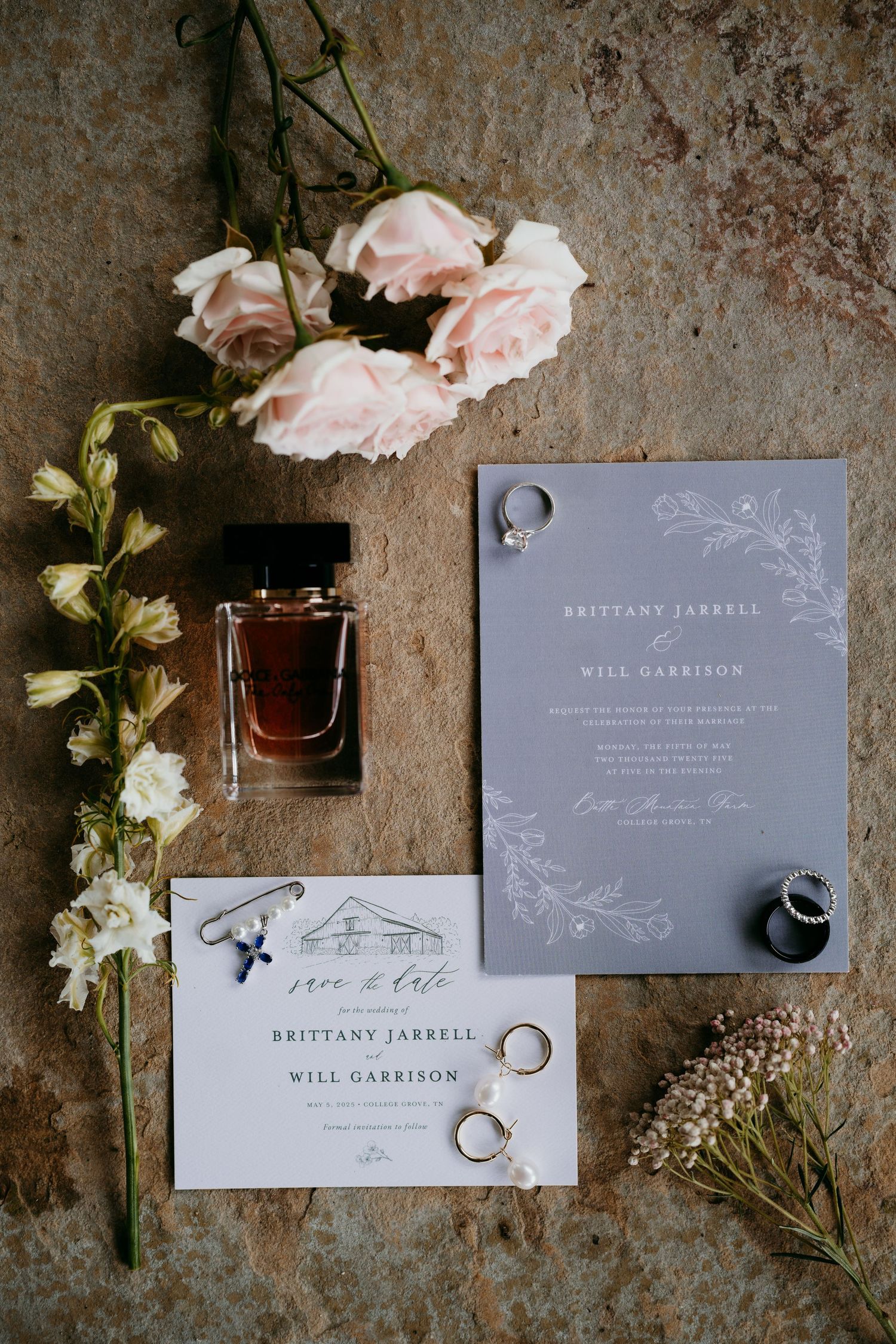 Wedding invitation suite with rings, perfume bottle and pink roses on textured surface at battle mountain farm in Nashville TN.