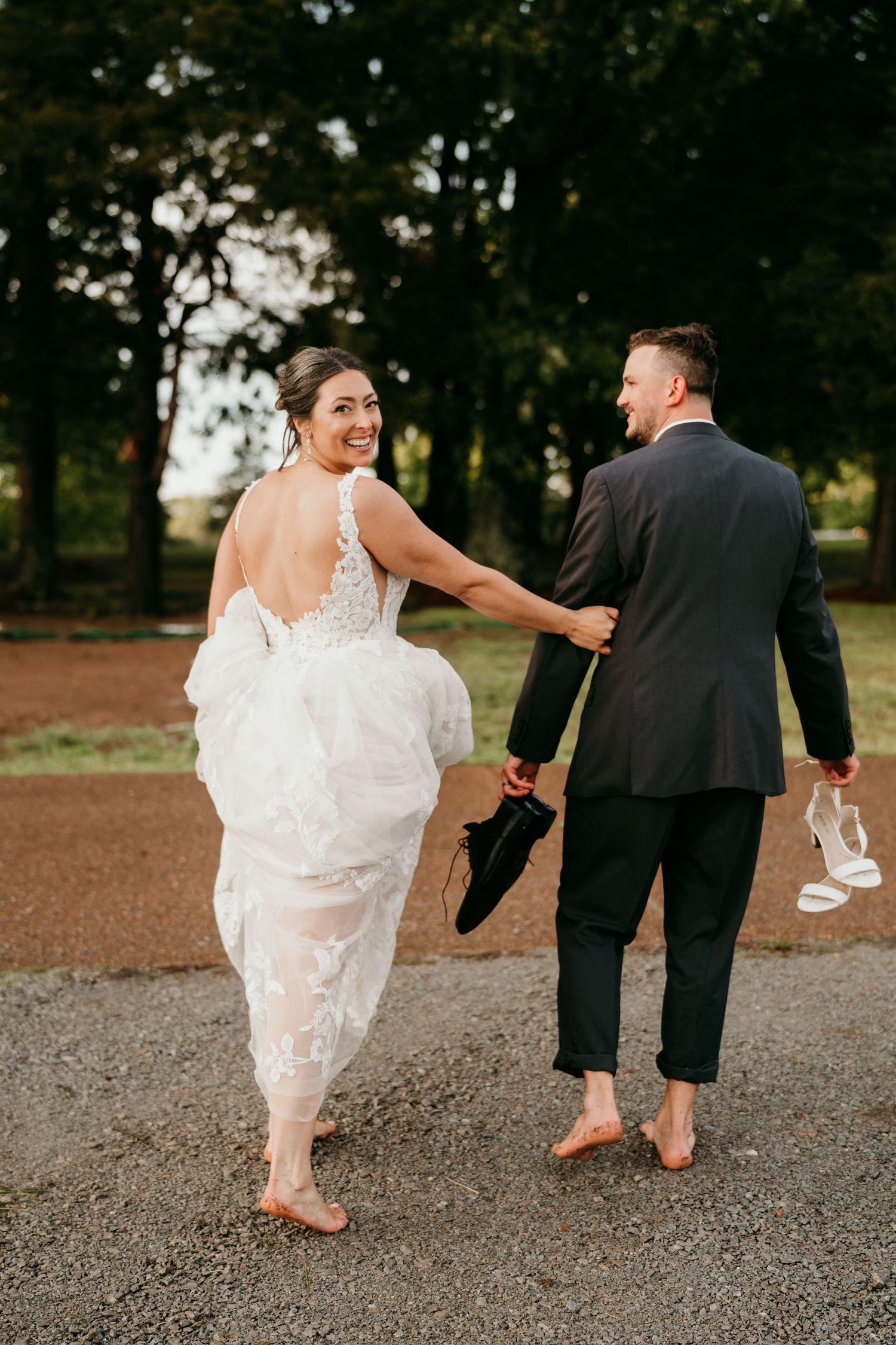 A bride and groom share a playful barefoot dance moment on a gravel path at an outdoor wedding venue.