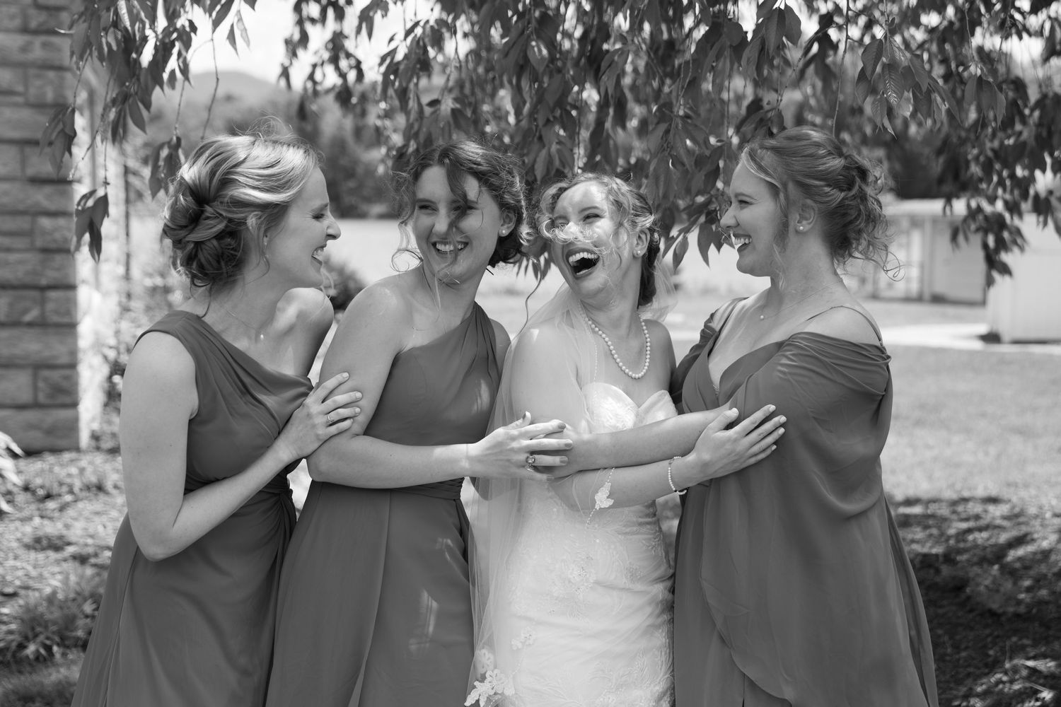 Wedding party members in gray dresses share laughs and candid moments outdoors.