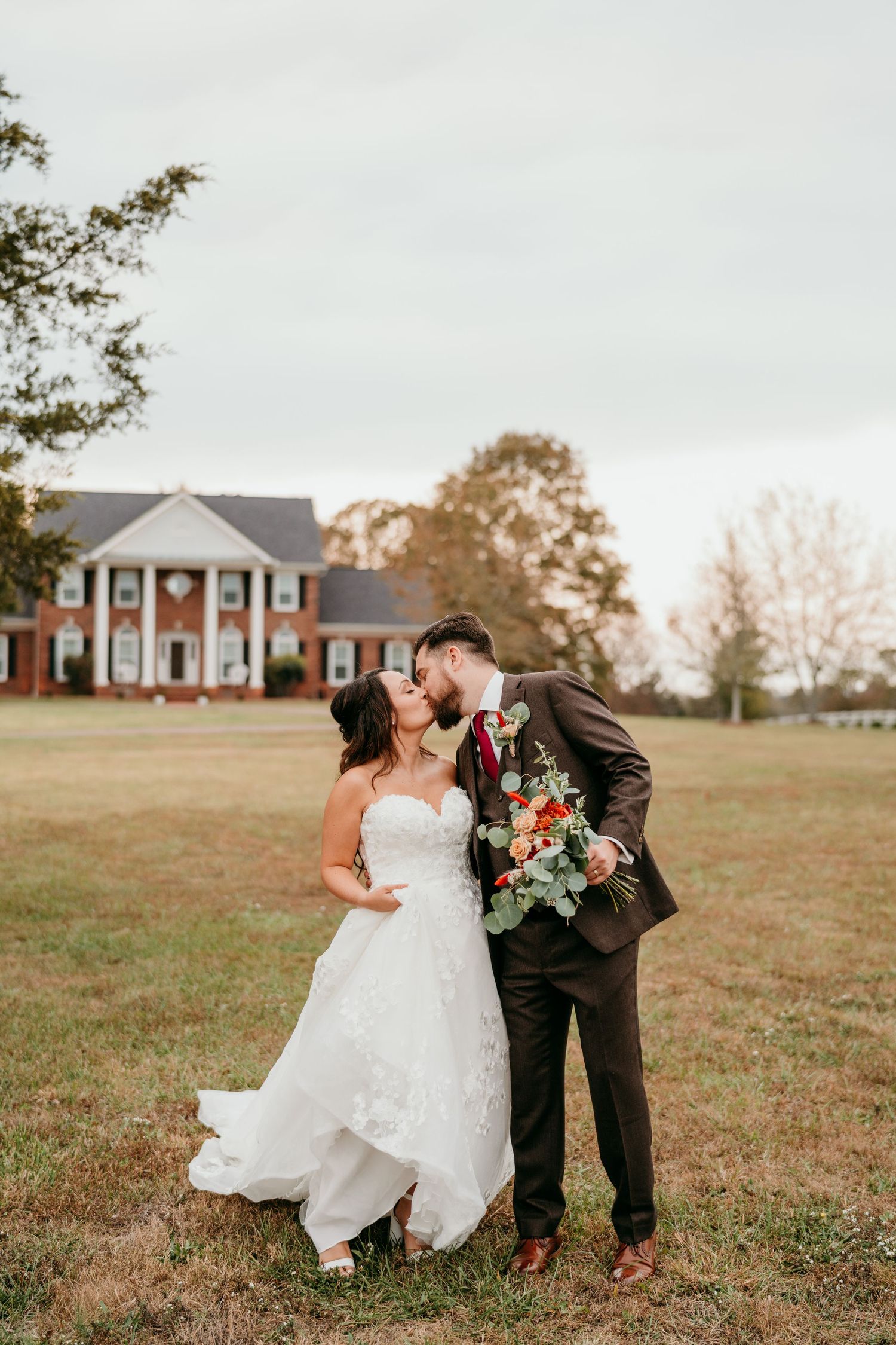 A romantic wedding portrait captured in front of a white pillared mansion with lush autumn grounds.