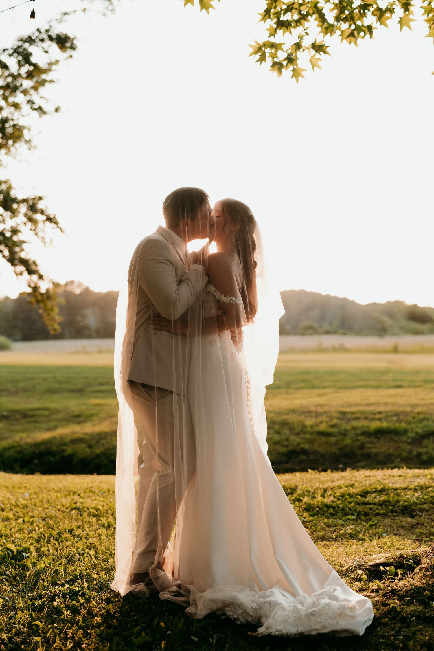 A romantic silhouette under the vail of a couple in wedding attire standing in a sun-drenched field at golden hour Nashville TN