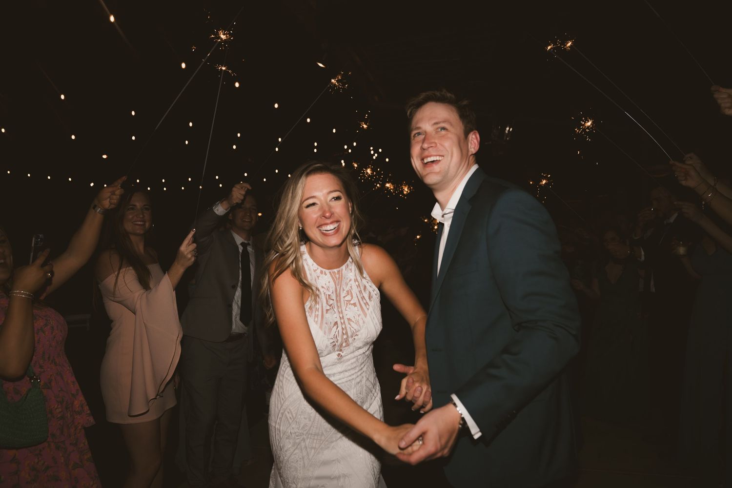 A couple dances joyfully together at a wedding reception with sparkling lights overhead.