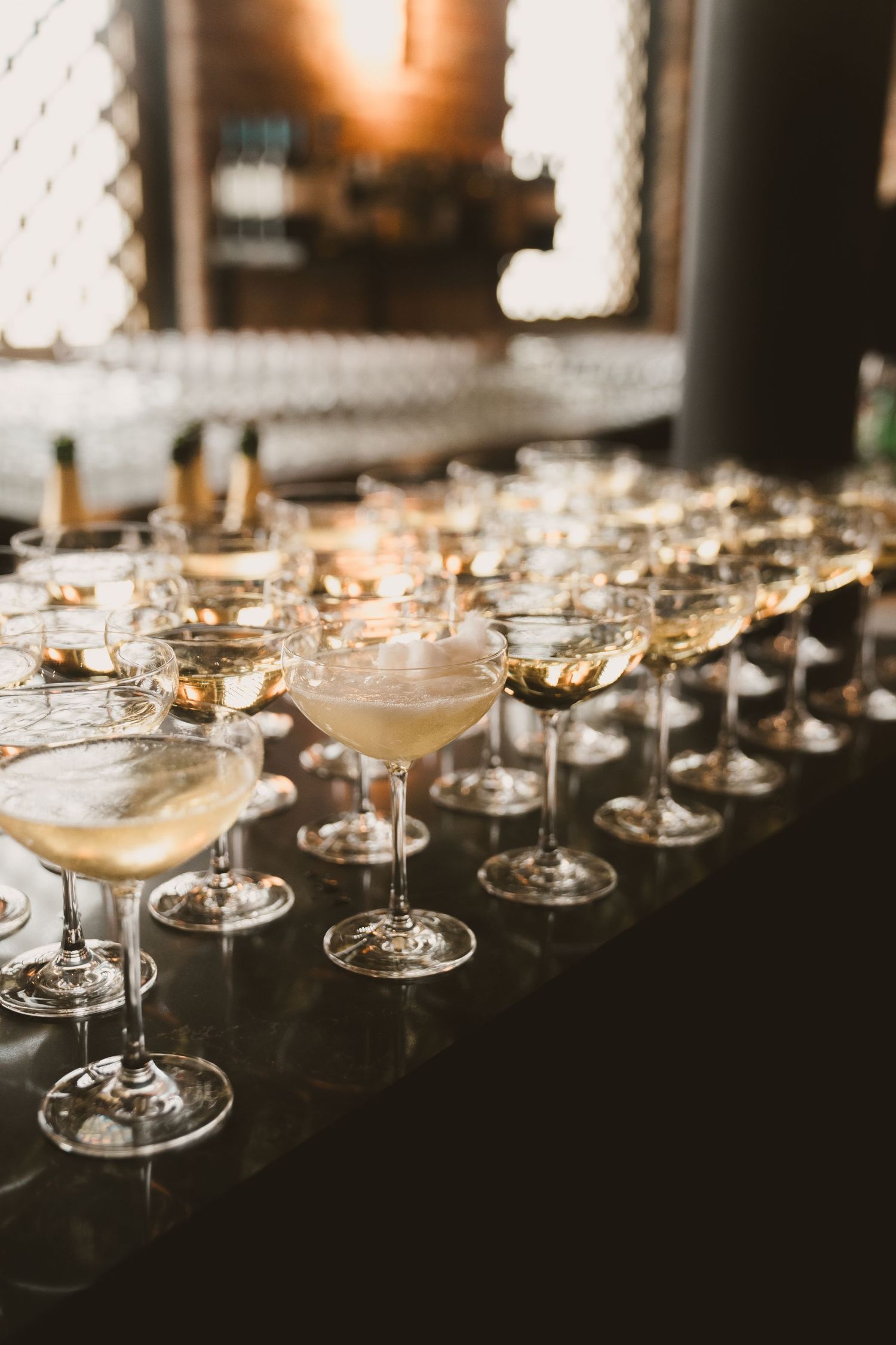 Elegant champagne coupes lined up on a dark bar filled with golden cocktails.