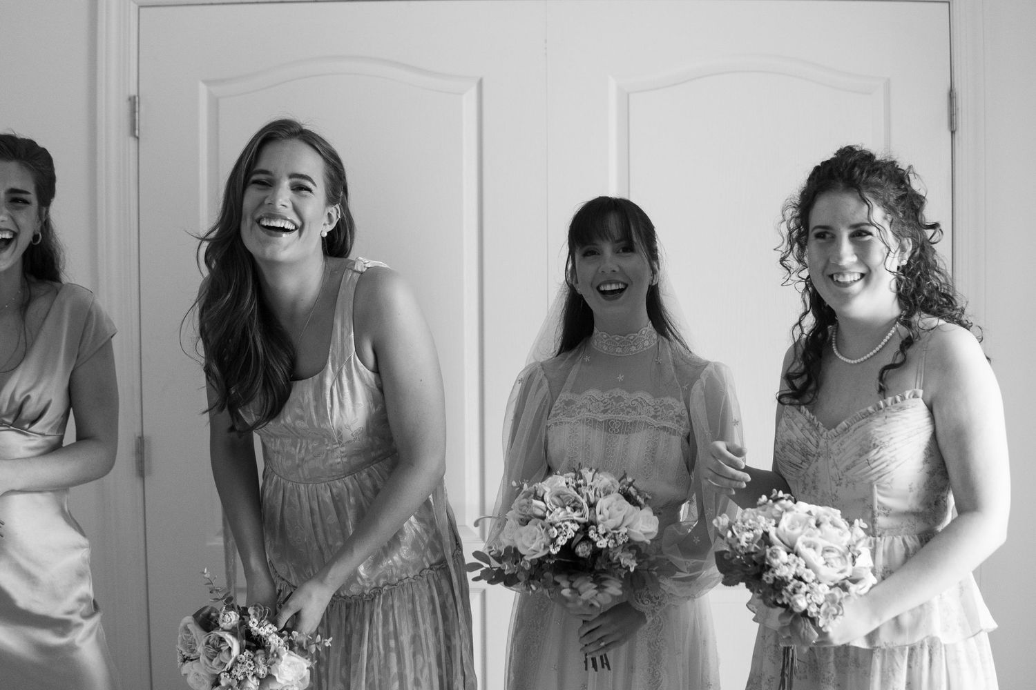 Bridesmaids in soft gray dresses smile and laugh together during wedding celebrations.