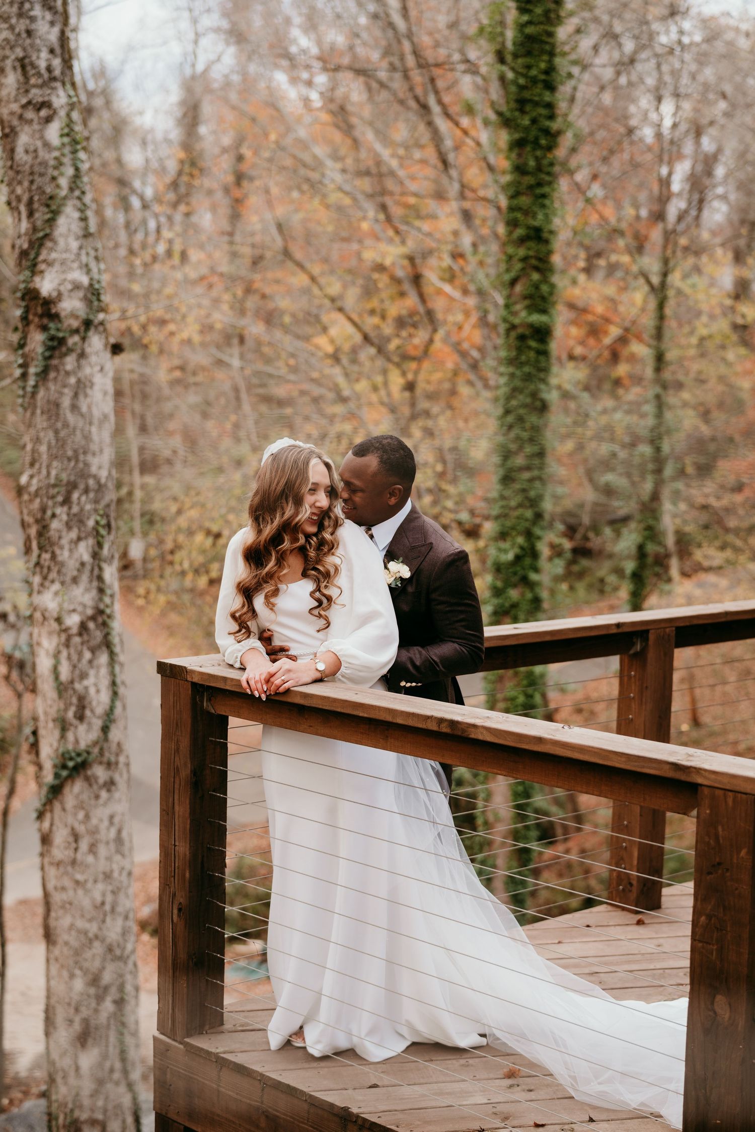 Romantic wedding couple sharing intimate moments on a wooden deck surrounded by autumn trees in the forest.