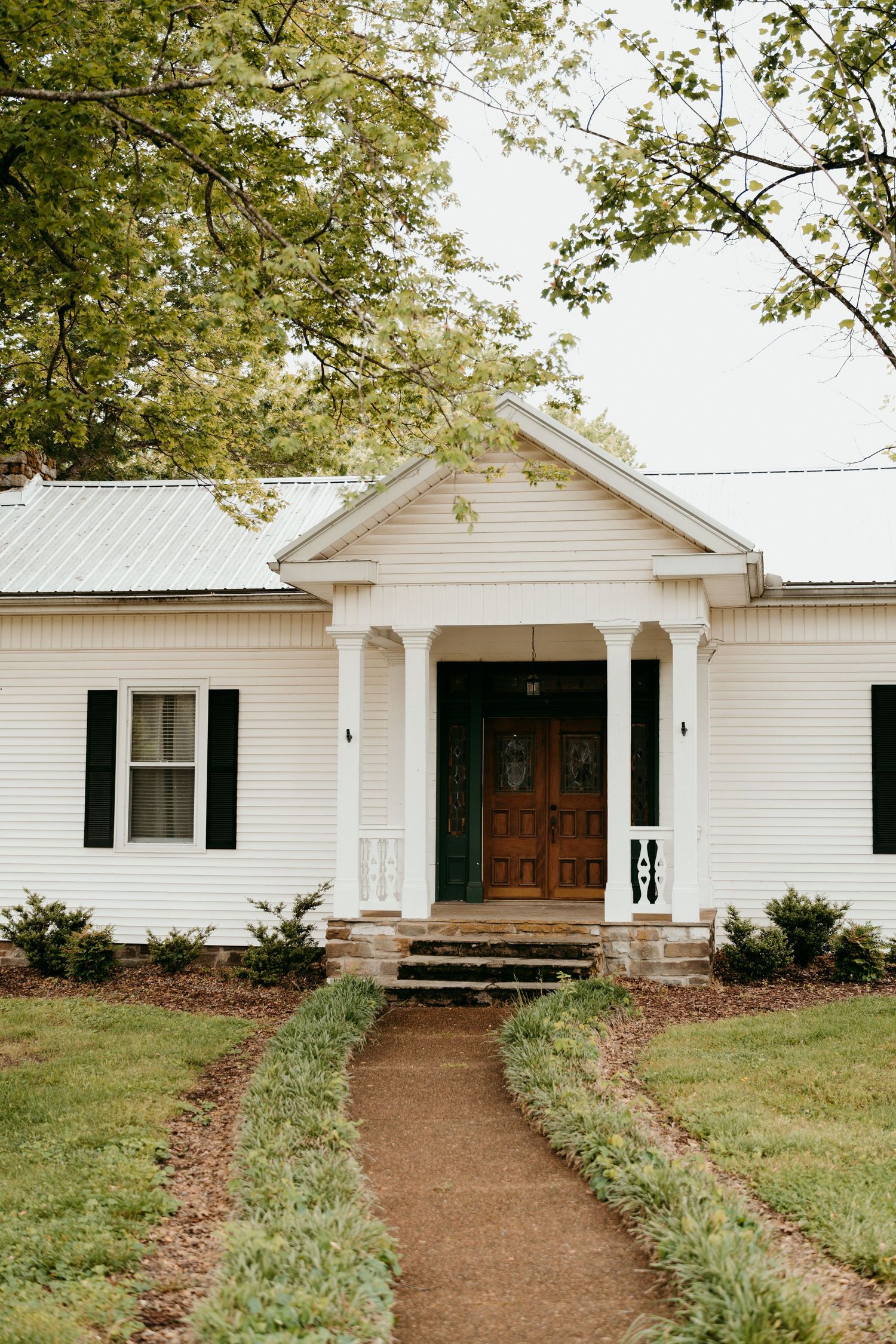 Classic white farmhouse with columned entrance and landscaped pathway at battle mountain farm in Nashville TN.