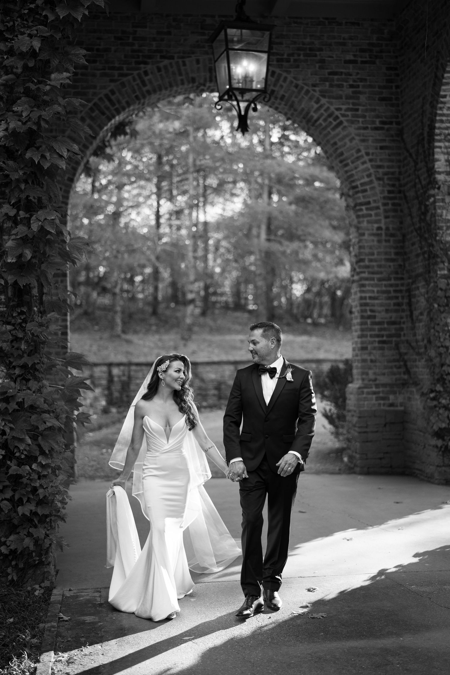 A couple walking under a romantic brick archway in formal wedding attire.
