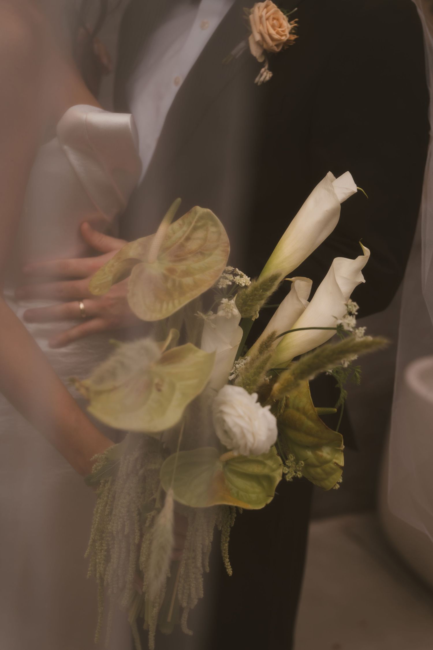 Close-up of wedding boutonniere with white calla lily and green anthurium leaves.