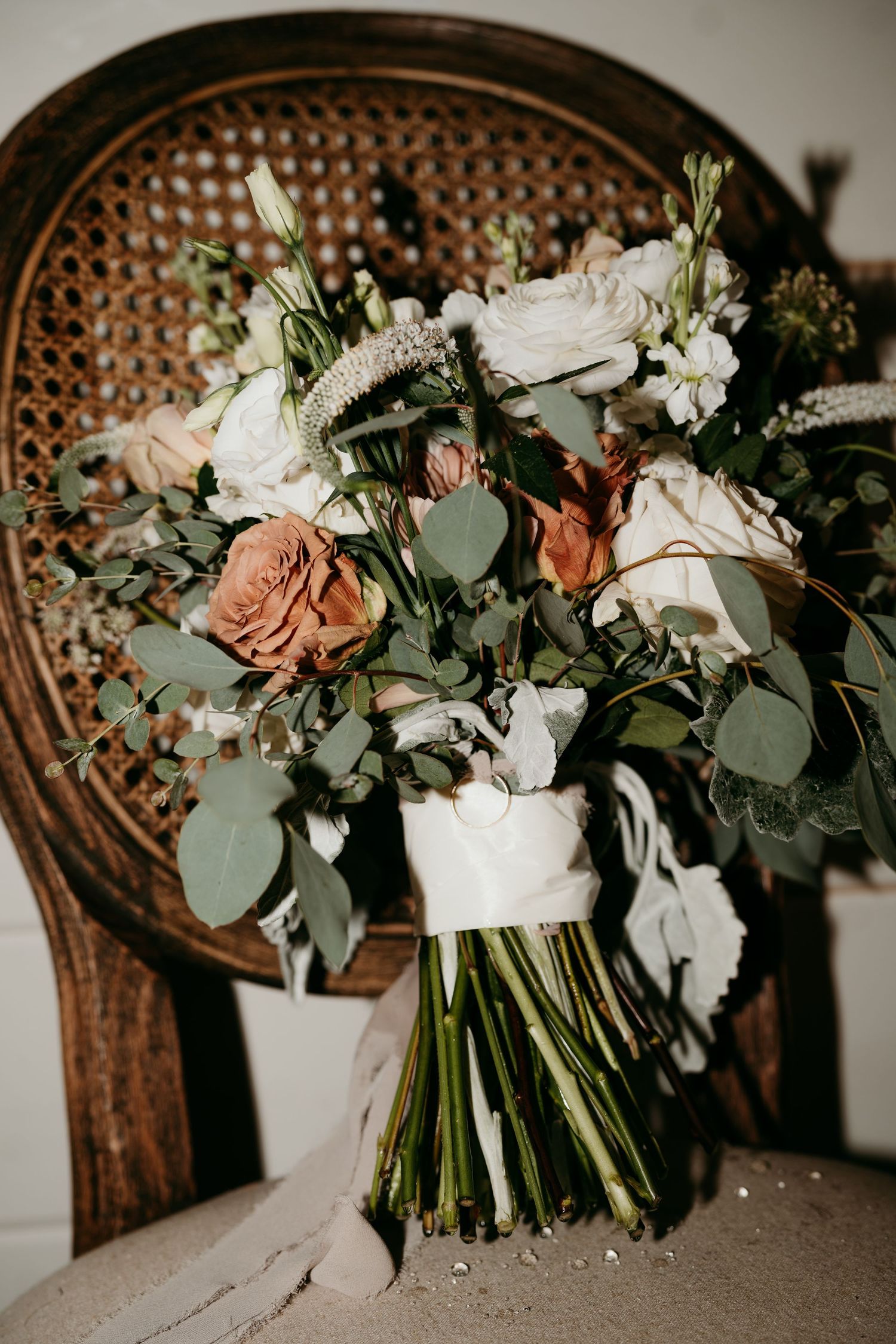 Romantic wedding bouquet with white roses, peach flowers and eucalyptus on vintage cane chair in Nashville TN