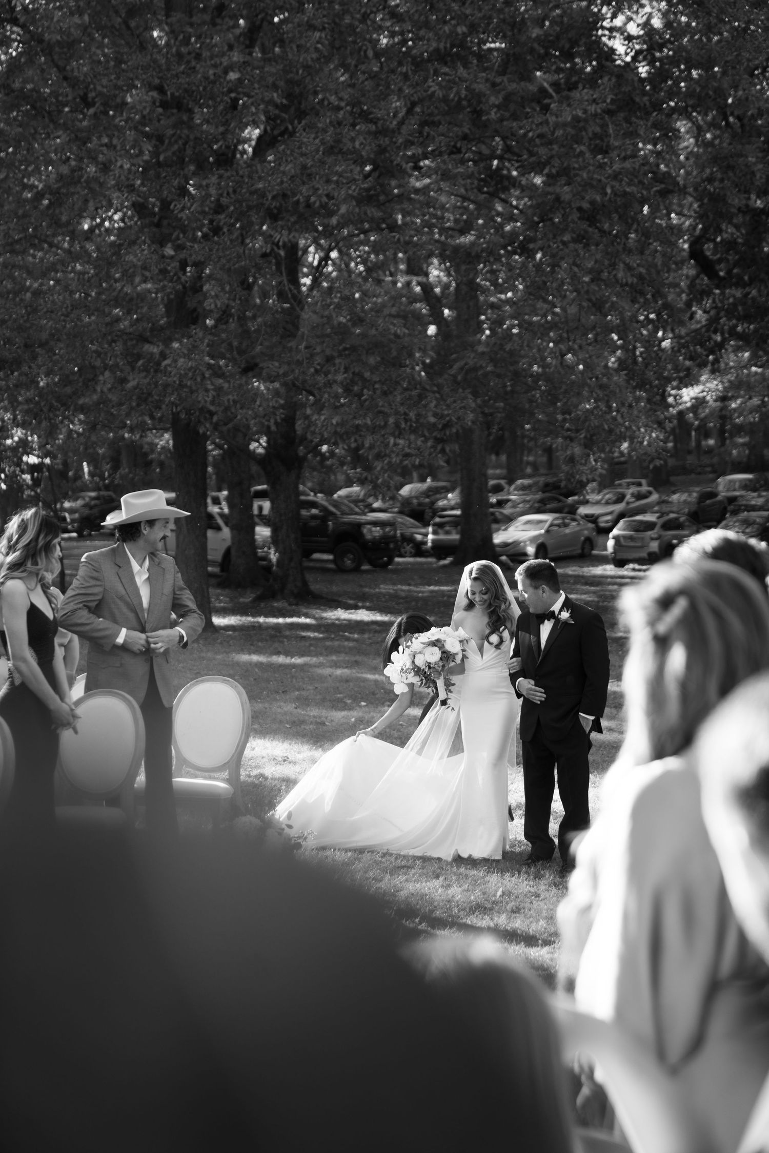 Black and white photograph of a bride in a flowing gown walking outside among trees during a wedding ceremony in Nashville TN