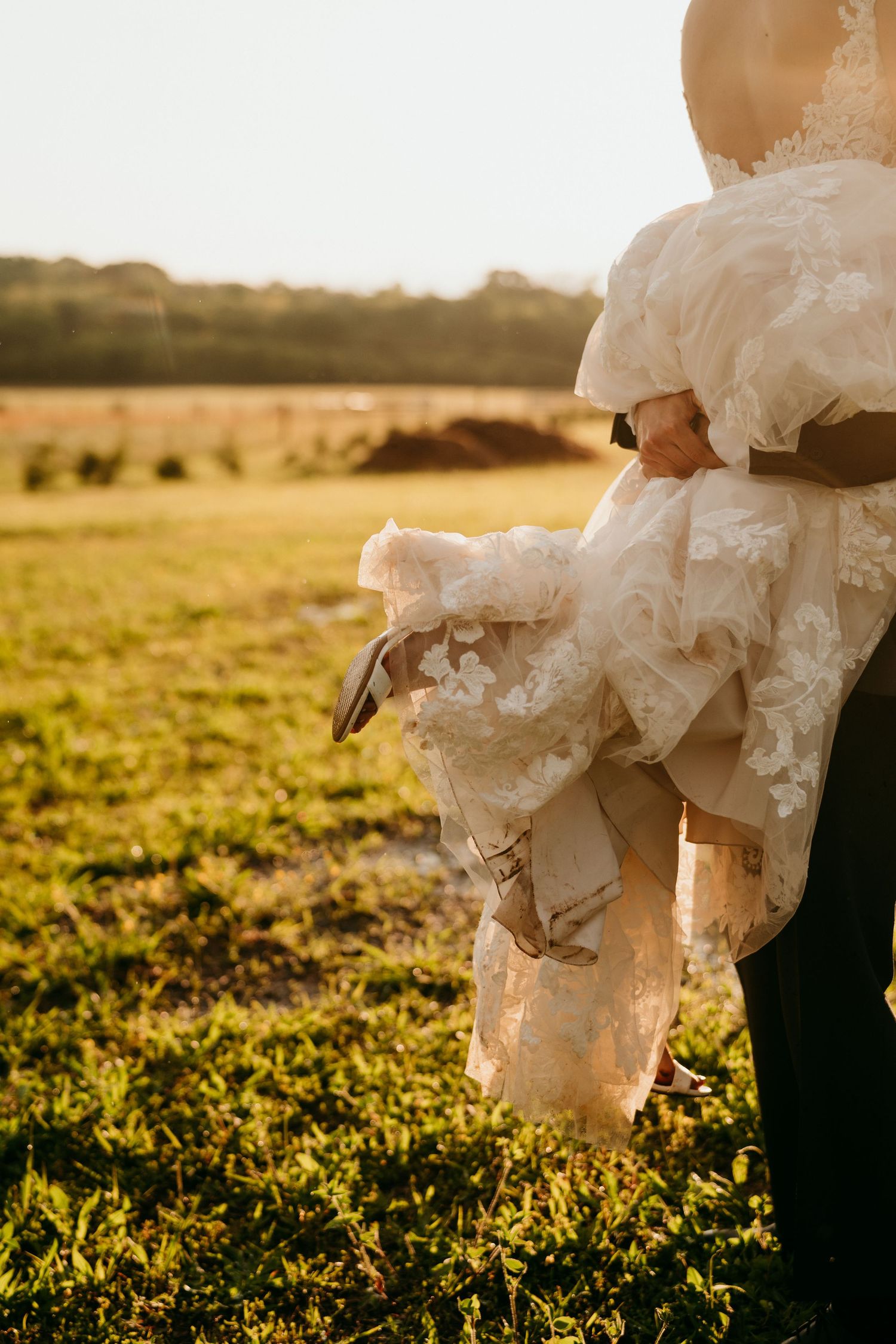 White wedding dress fabric billows in golden sunlight across a grassy field during sunset.