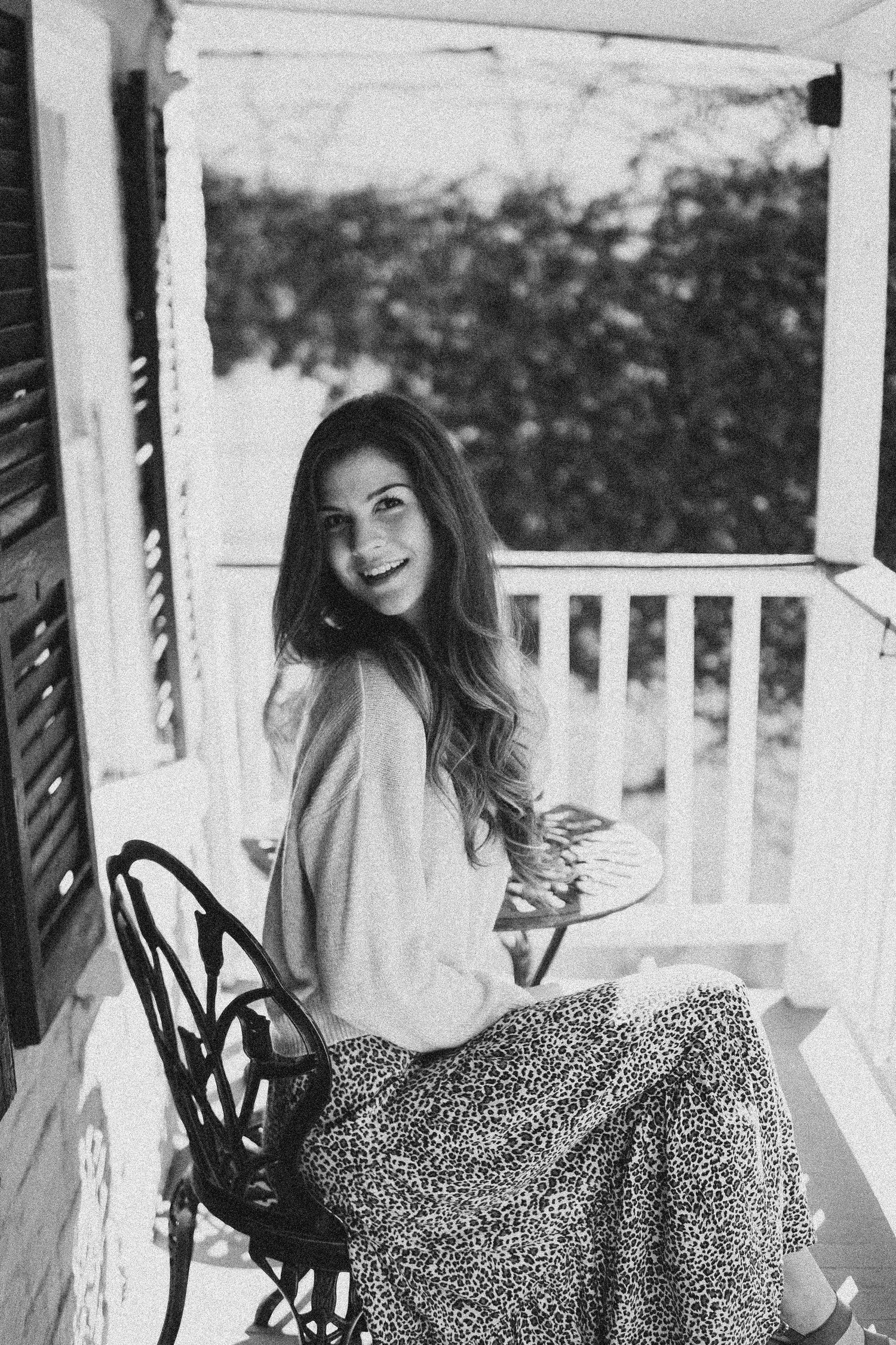 Black and white portrait of woman in flowing skirt sitting on porch chair in Nashville TN