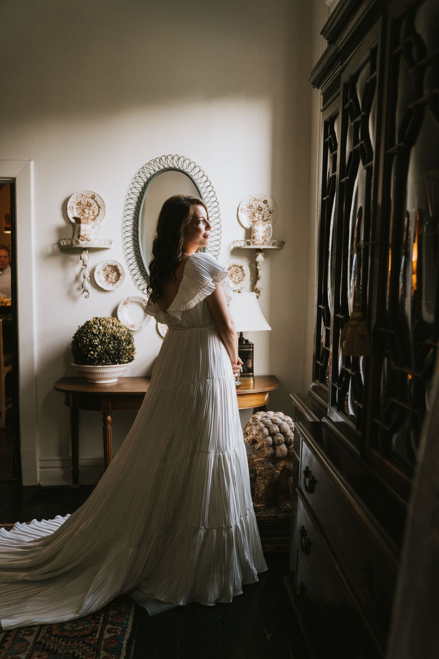 A flowing white wedding gown creates dramatic shadows in an elegantly decorated room.