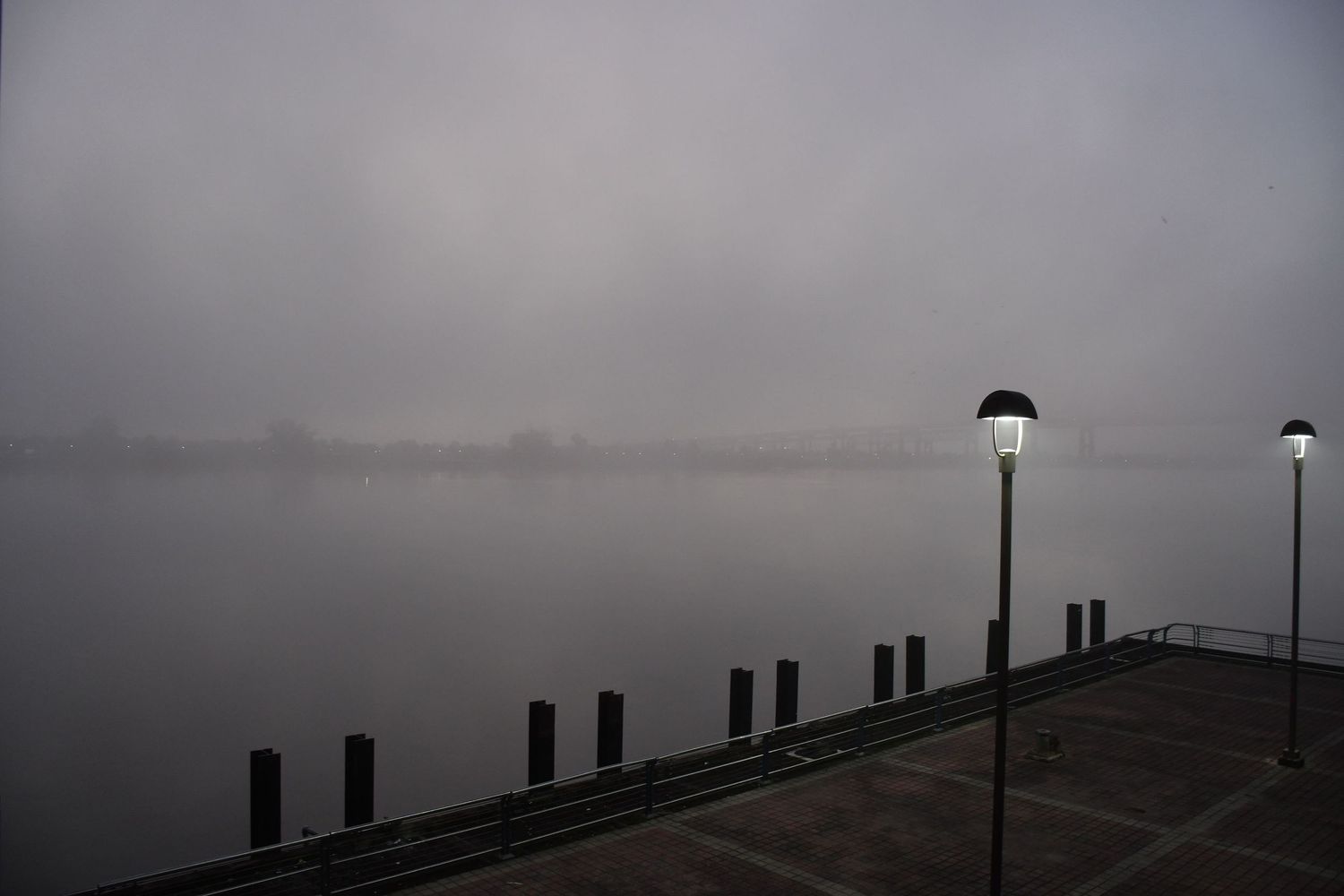 Row of silhouetted fence posts and lampposts along a path on an overcast foggy day.