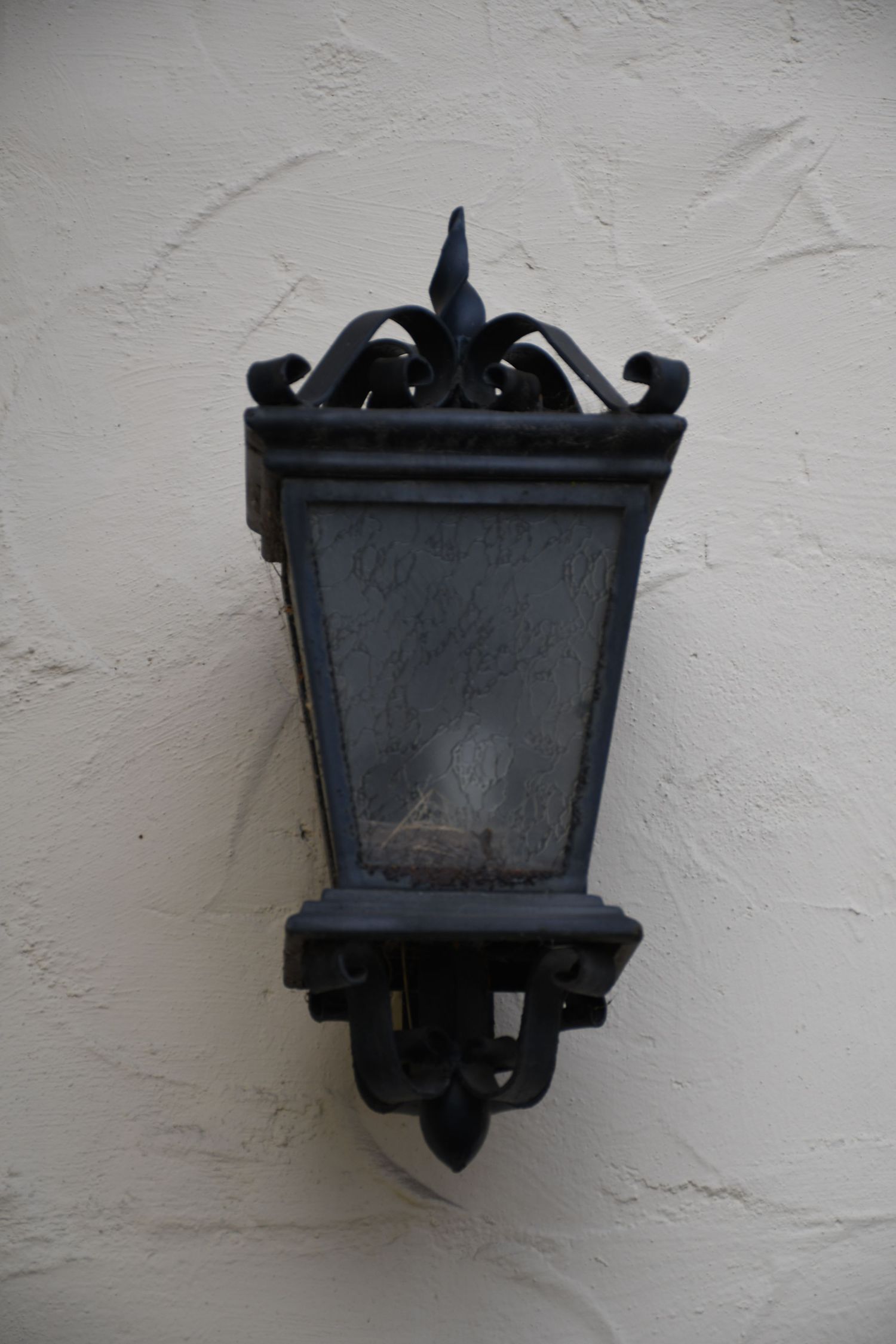 A black ornate vintage wall lantern mounted on a textured white wall.