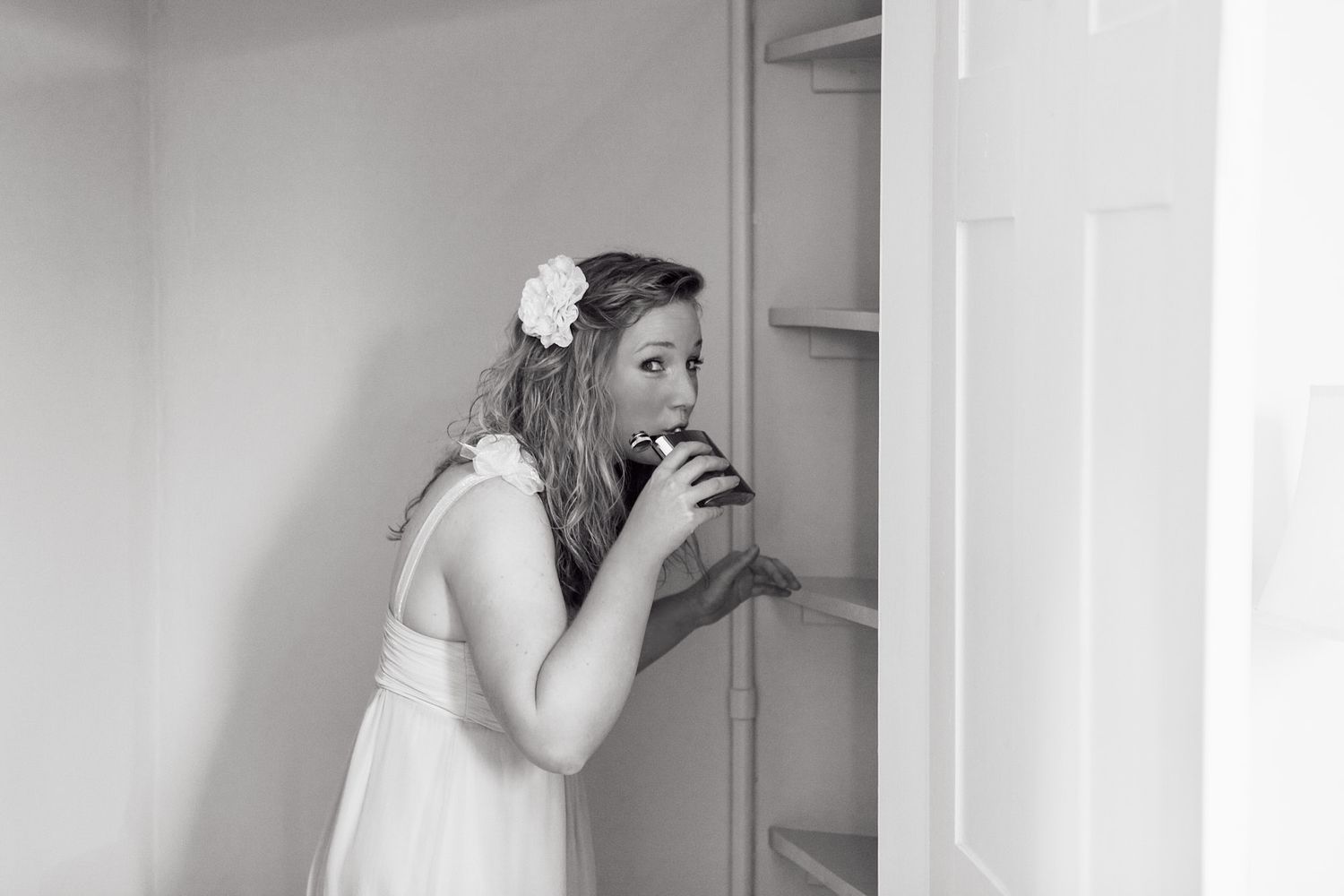 Black and white photo of bridesmaid in white dress drinking from a hip-flask.