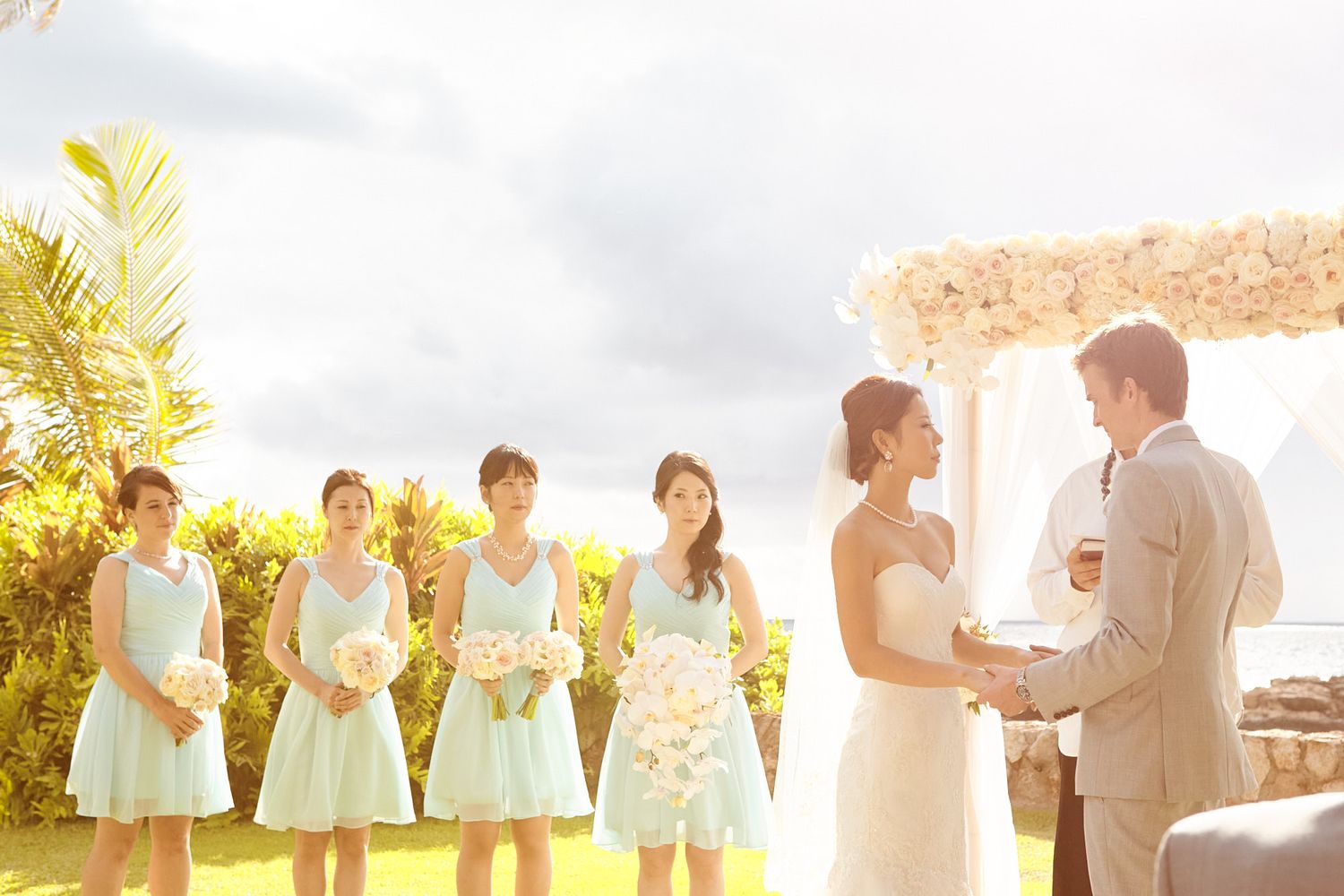 Wedding party poses in soft sunlight against outdoor backdrop wearing mint green dresses and beige suits.
