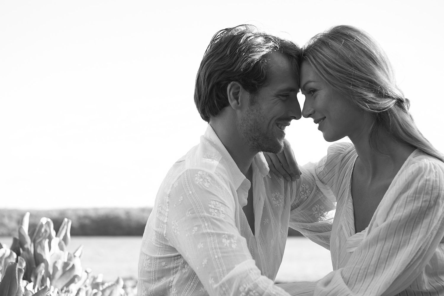 Black and white romantic engagement photoshoot of couple in white clothing outdoors.