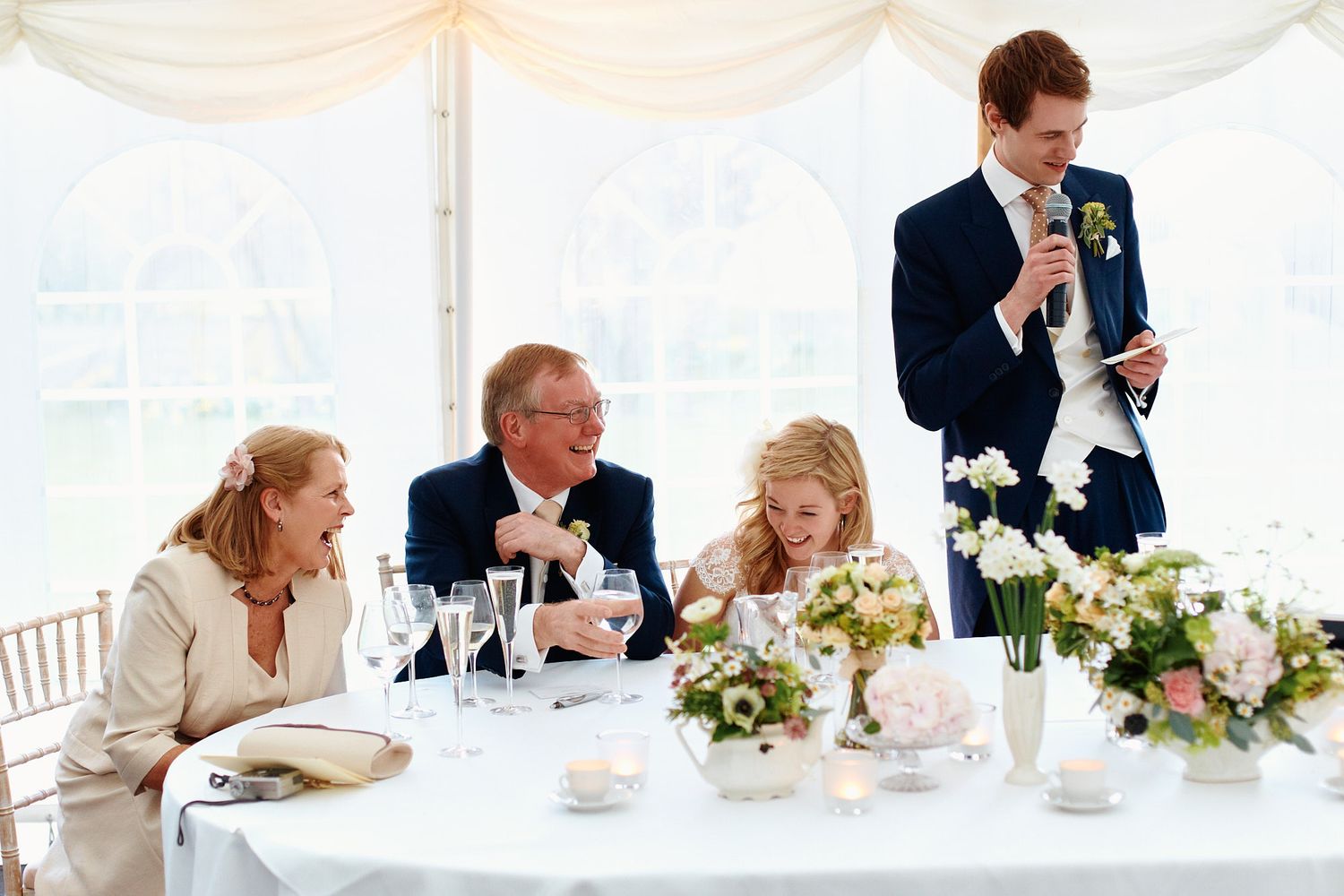 Wedding reception table settings under white marquee tent with floral centerpieces.