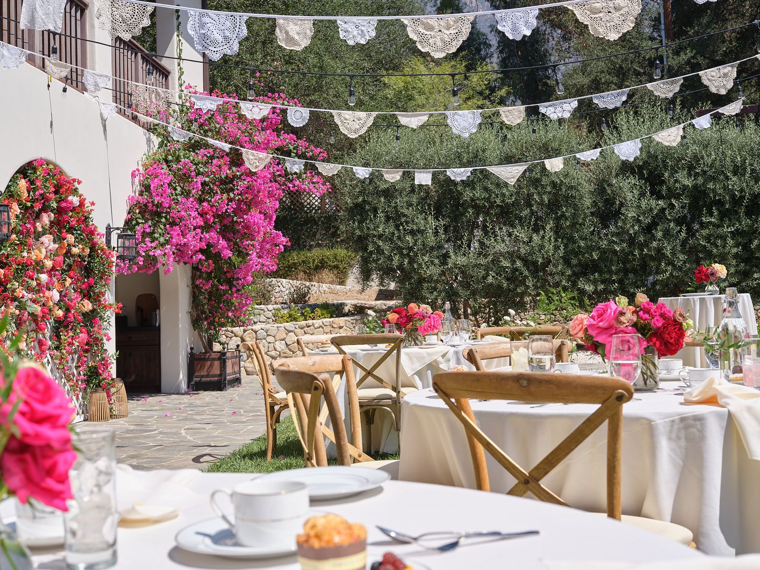 Outdoor wedding reception tables decorated with pink flowers and vintage lace bunting.