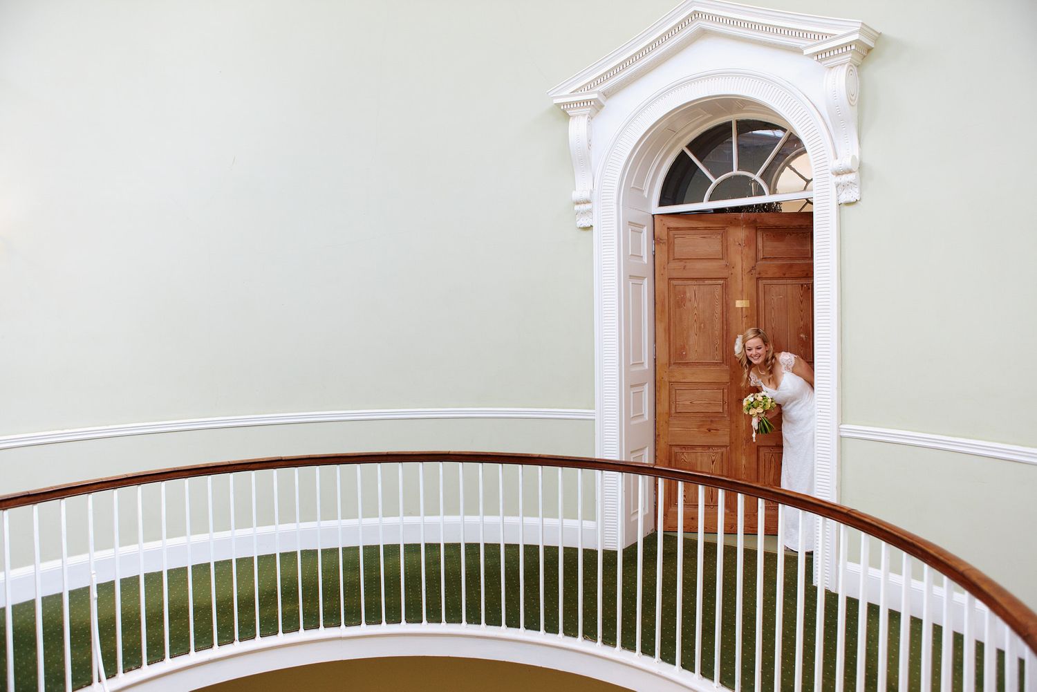 Elegant curved staircase with white walls and wooden banister leading to an arched doorway.
