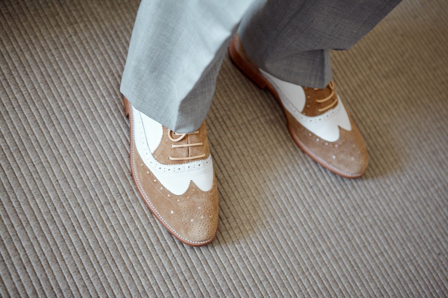Close-up view of elegant groom's shoes and ankles on a carpeted floor.