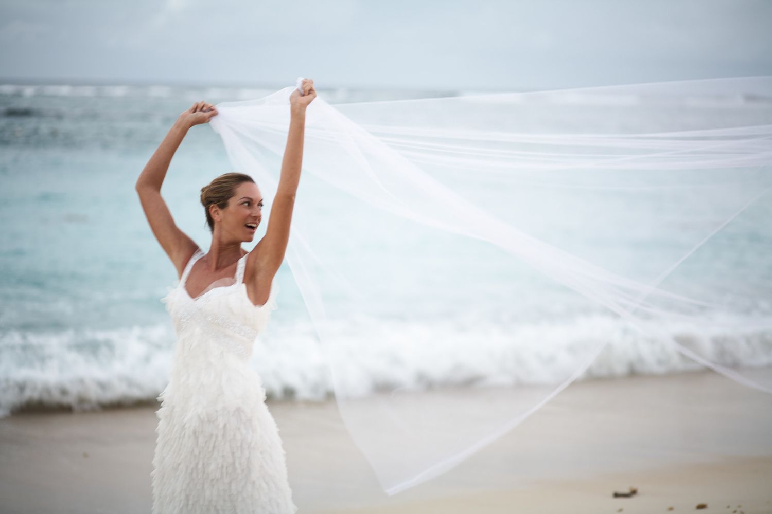 Bride in white dress celebrates joyfully on scenic beach shoreline in Mauritius on destination wedding.