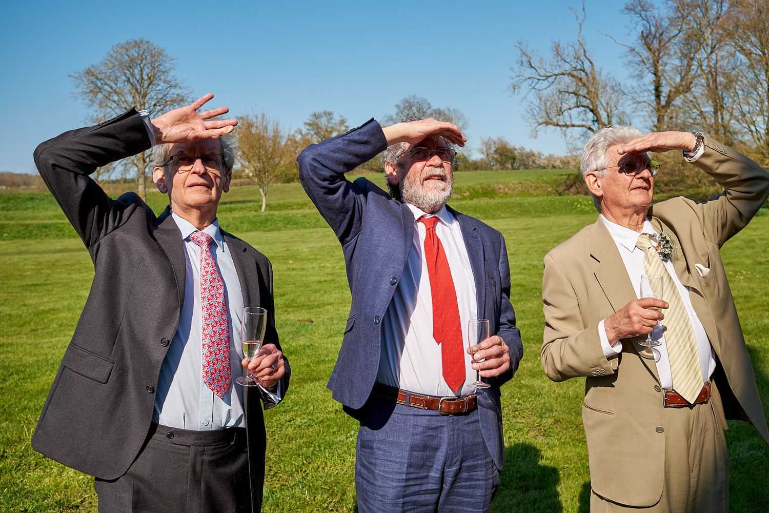Groomsmen looking into the distance on a grassy hilltop wearing suits and ties.
