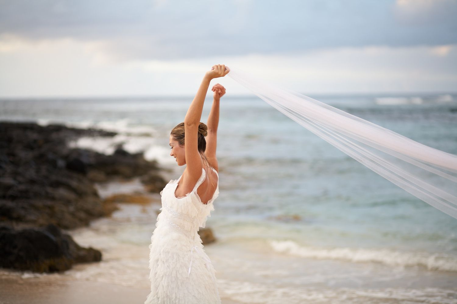 A bride in a white gown twirls with her veil blowing in the ocean breeze in Mauritius on destination wedding.