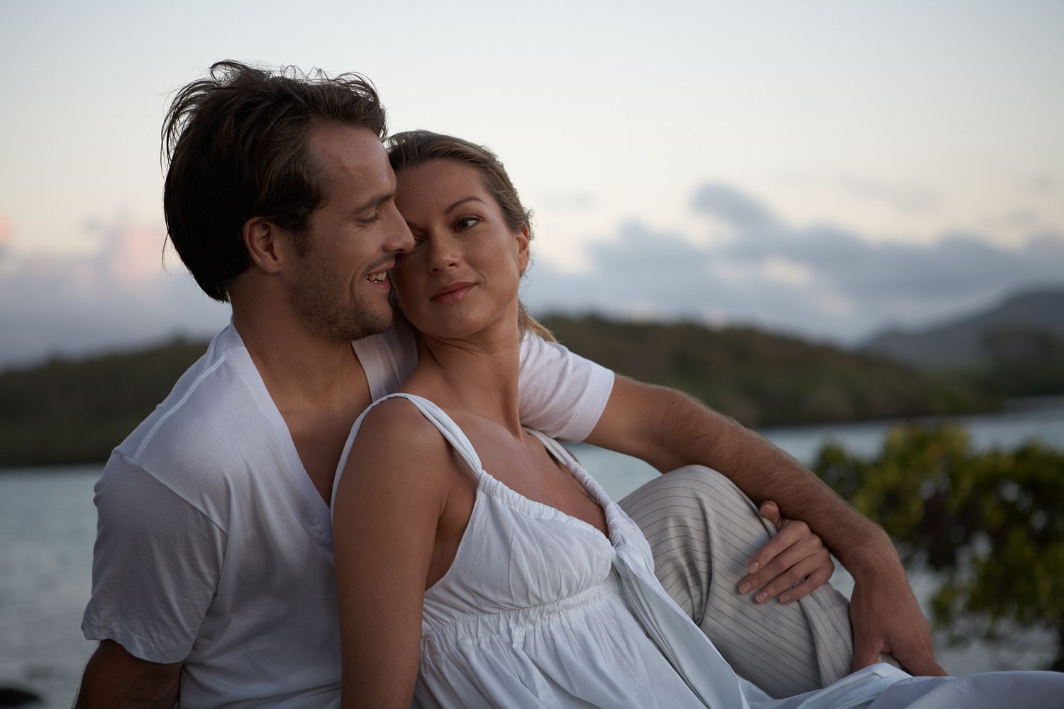 Romantic couple embracing during sunset with ocean and mountains in background in Mauritius on destination wedding.