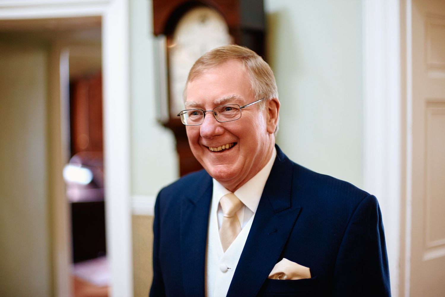Father of the bride in a navy suit and gold tie smiles warmly in an indoor setting.