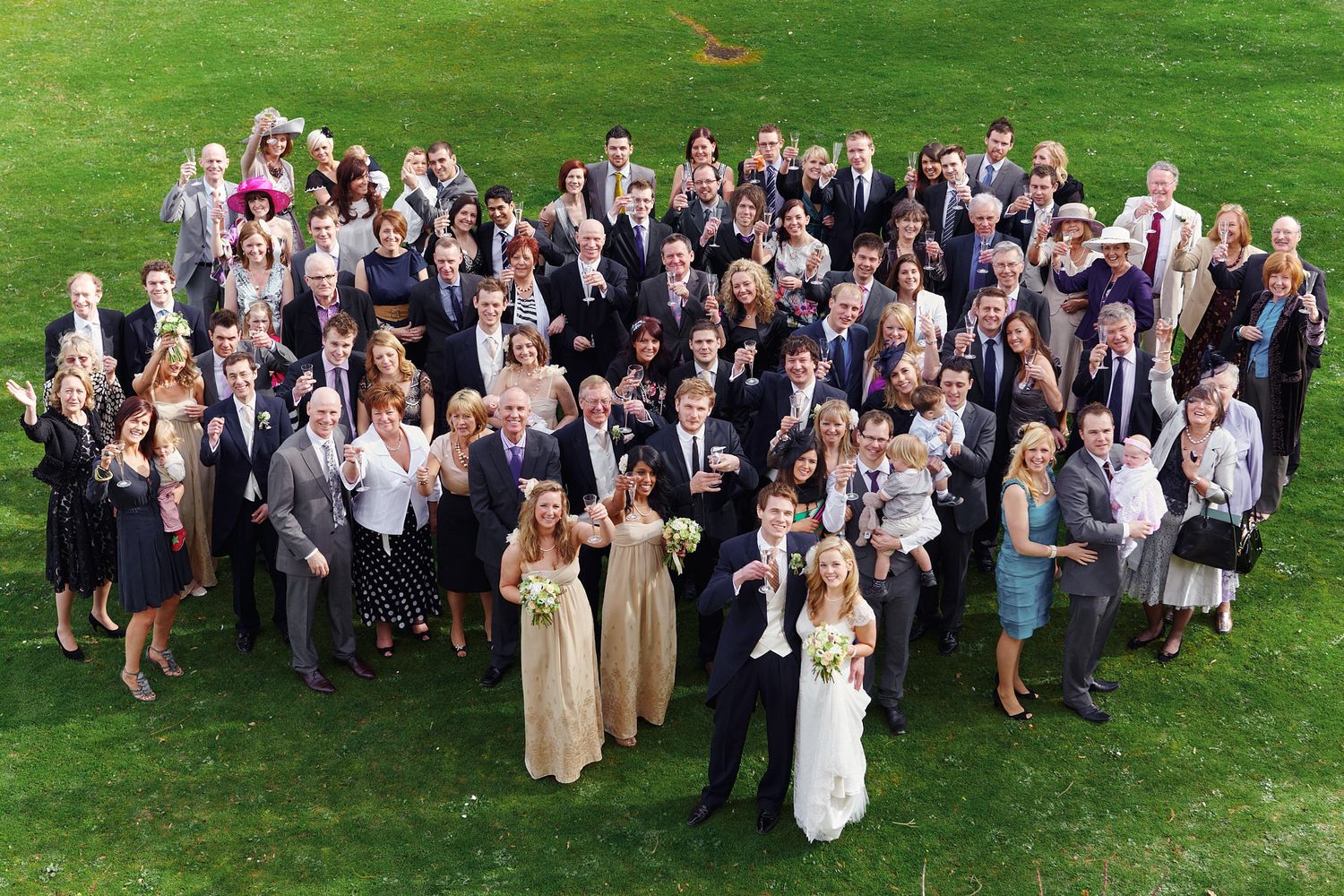 Large wedding party group photo on a grassy lawn.
