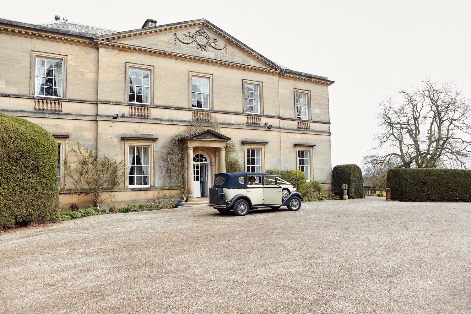 Exterior view of grand historic manor house with gravel driveway and manicured grounds.