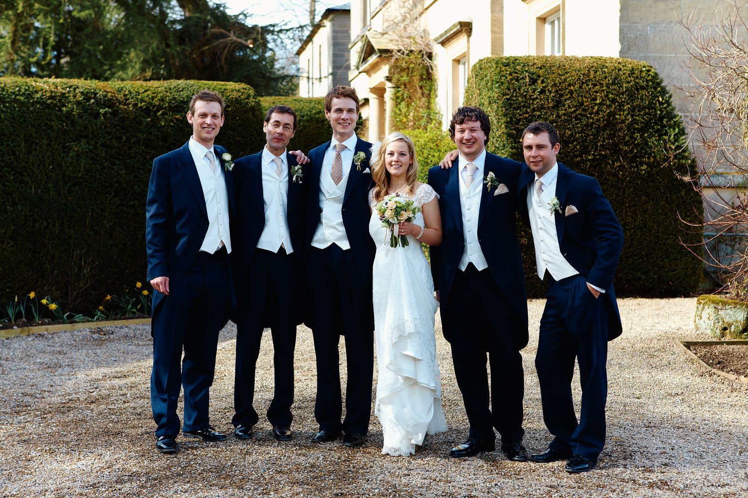 Wedding party in navy suits and formal attire posed outside historic stone building.