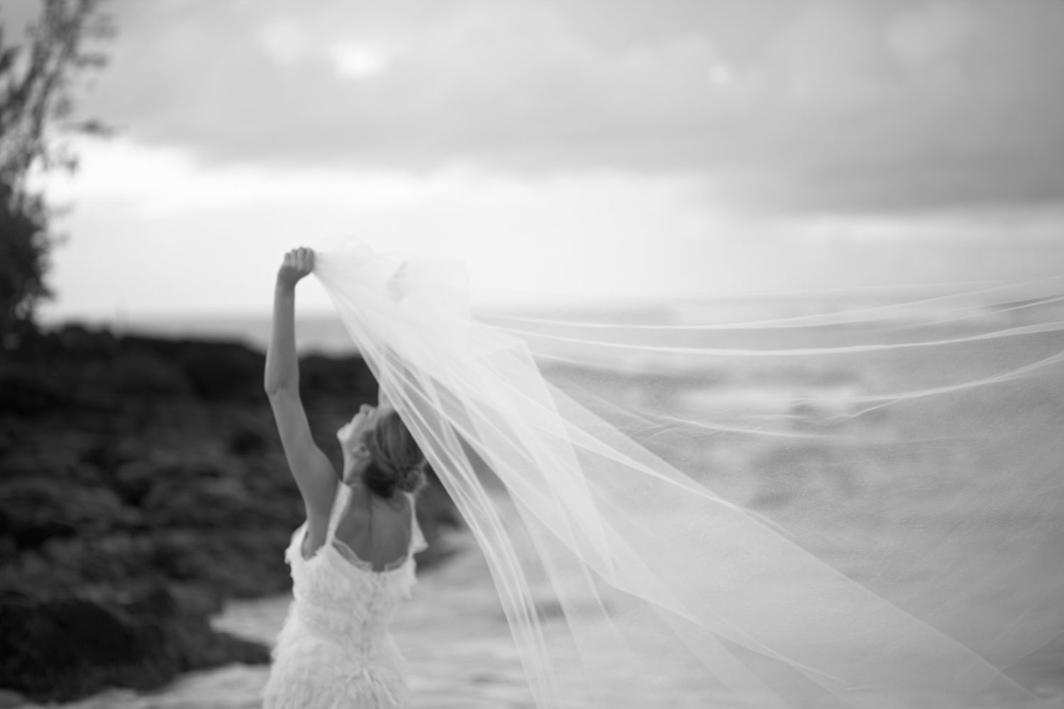 Wind catches bridal veil dramatically against cloudy coastal landscape in Mauritius on destination wedding.