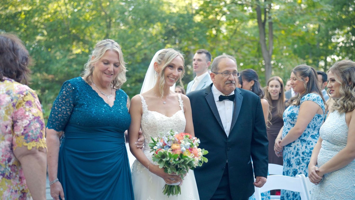 Bride walking down aisle with parents during outdoor Arrow Park wedding ceremony.